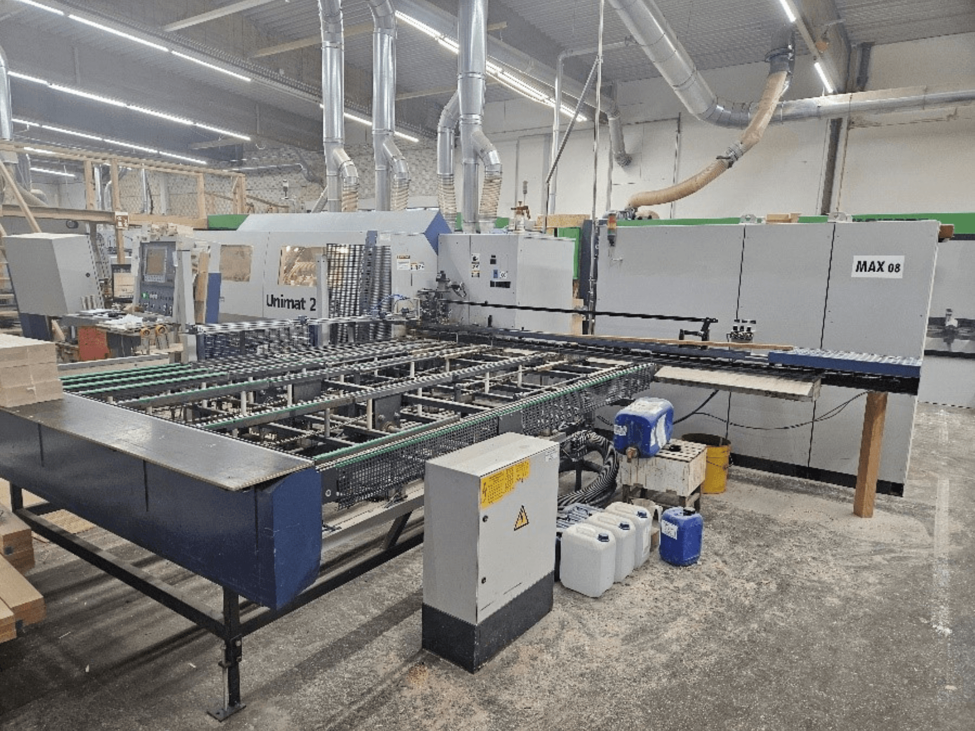 Bir atölyedeki Unimat 2 CNC makinesinin yandan görünümü, konveyör bantları ve görünür Max 08 ünitesi ile teknik bileşenler.
