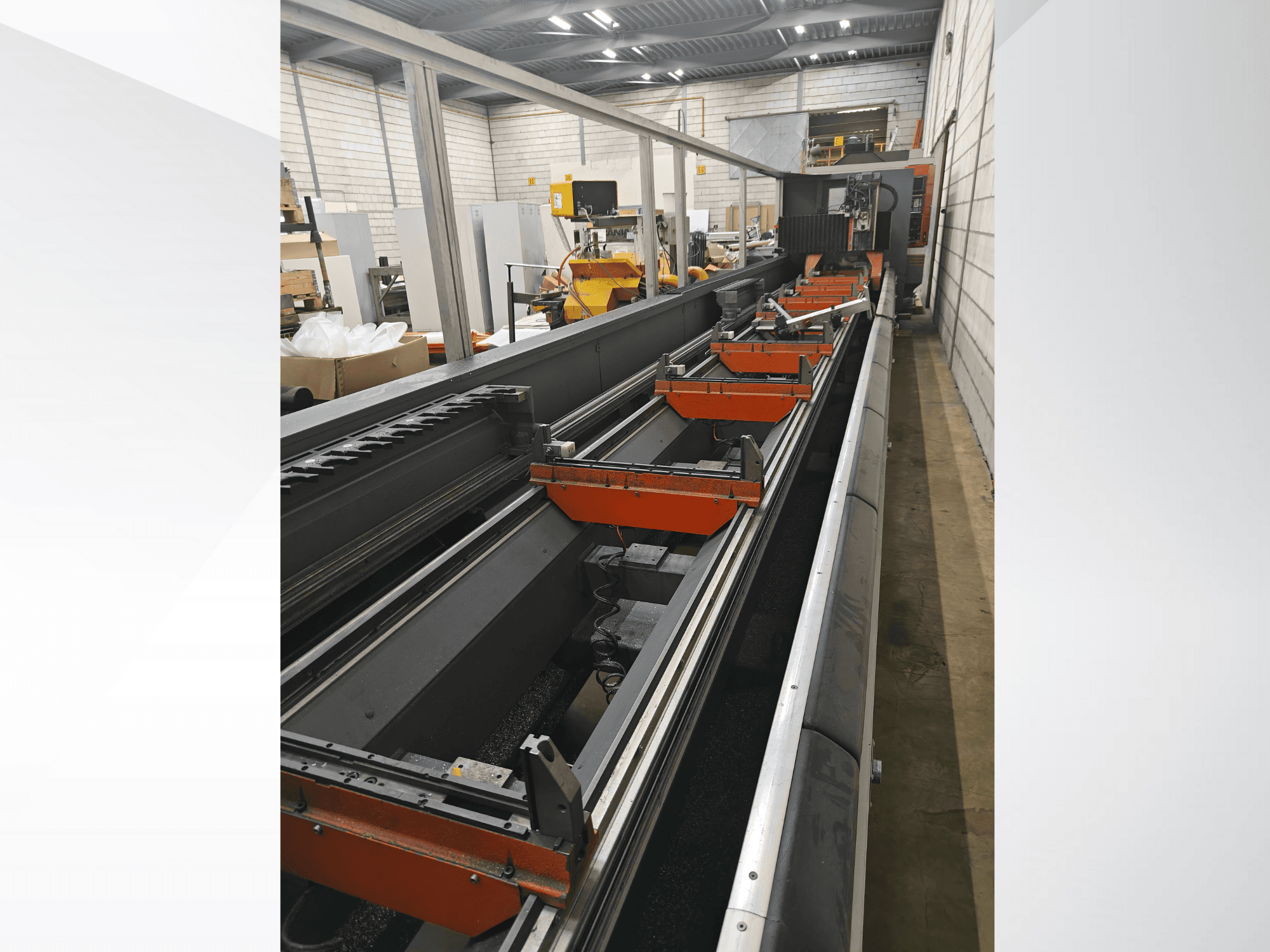 Bir depo ortamında doğrusal raylar, turuncu kelepçeler ve hassas bileşenler içeren endüstriyel CNC makinesi yan görünümü.