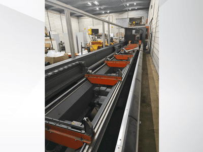 Bir depo ortamında doğrusal raylar, turuncu kelepçeler ve hassas bileşenler içeren endüstriyel CNC makinesi yan görünümü.