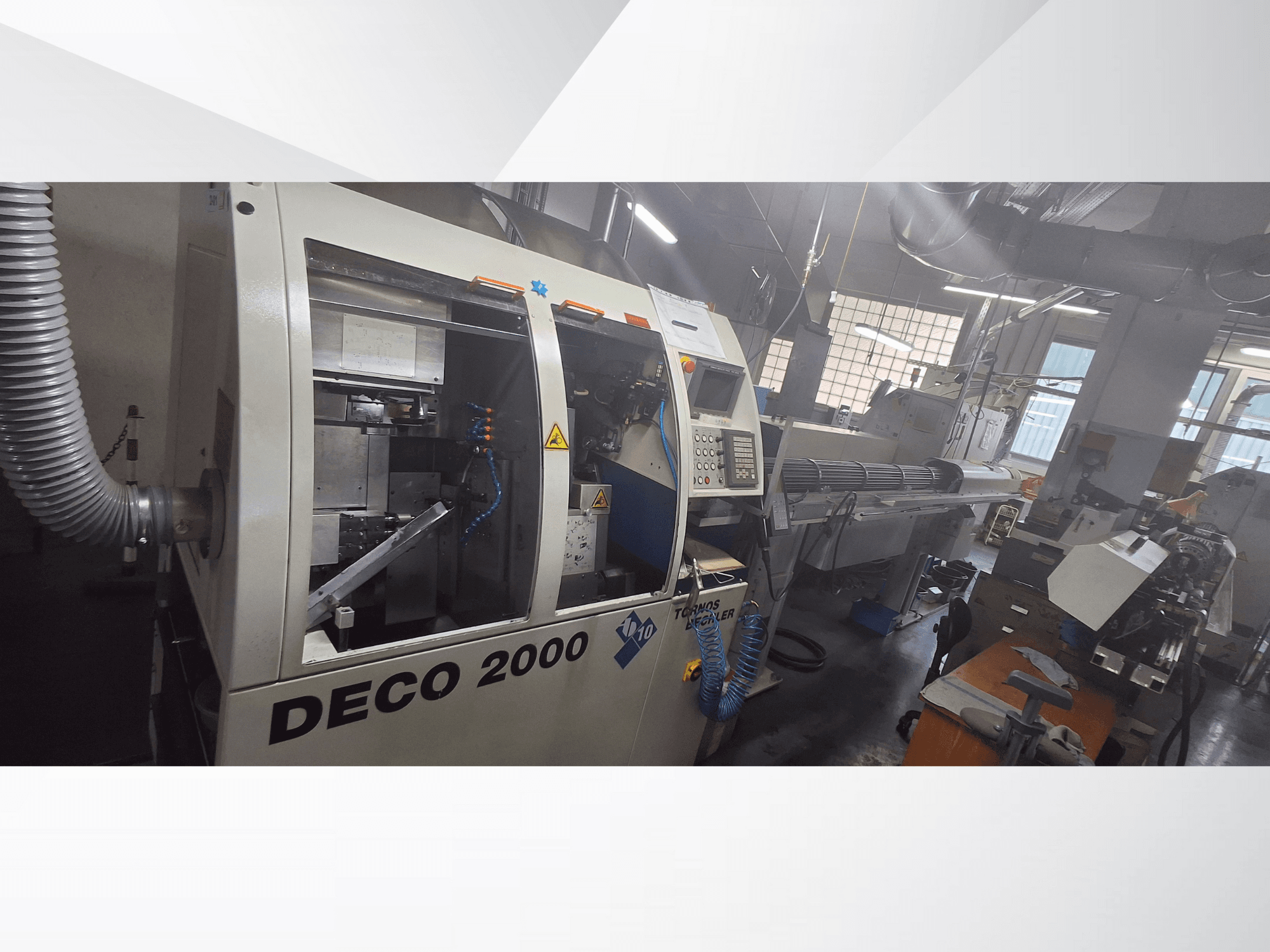 DECO 2000 CNC makinesi bir atölyede, önden görünüm, kontrolleri ve sağda uzun bir iş parçası kurulumunu sergiliyor.