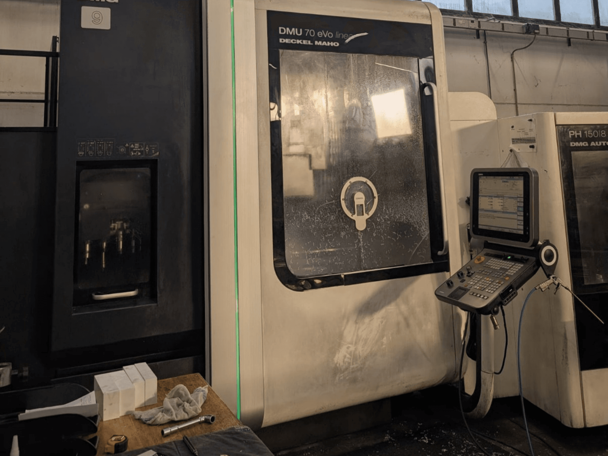 DMG DECKEL MAHO DMU 70 EVO Lineer dik işleme merkezi, kontrol paneli, takımlar ve çalışma alanı görünür şekilde önden görünüm.