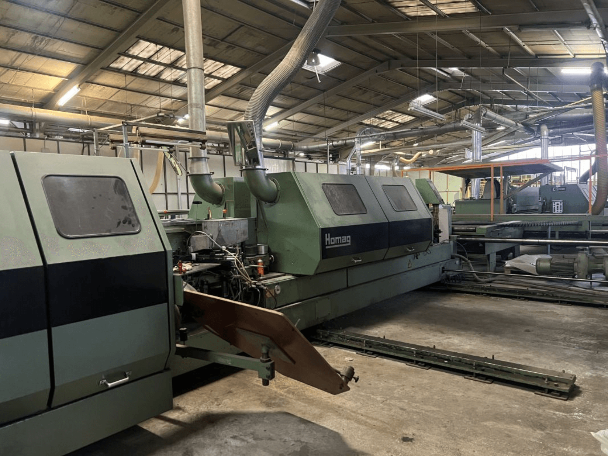 Yeşil renkli Homag endüstriyel makine, yandan görünüm, operasyonel bileşenler ve kontrol paneli bir depo ortamında görülebilir.