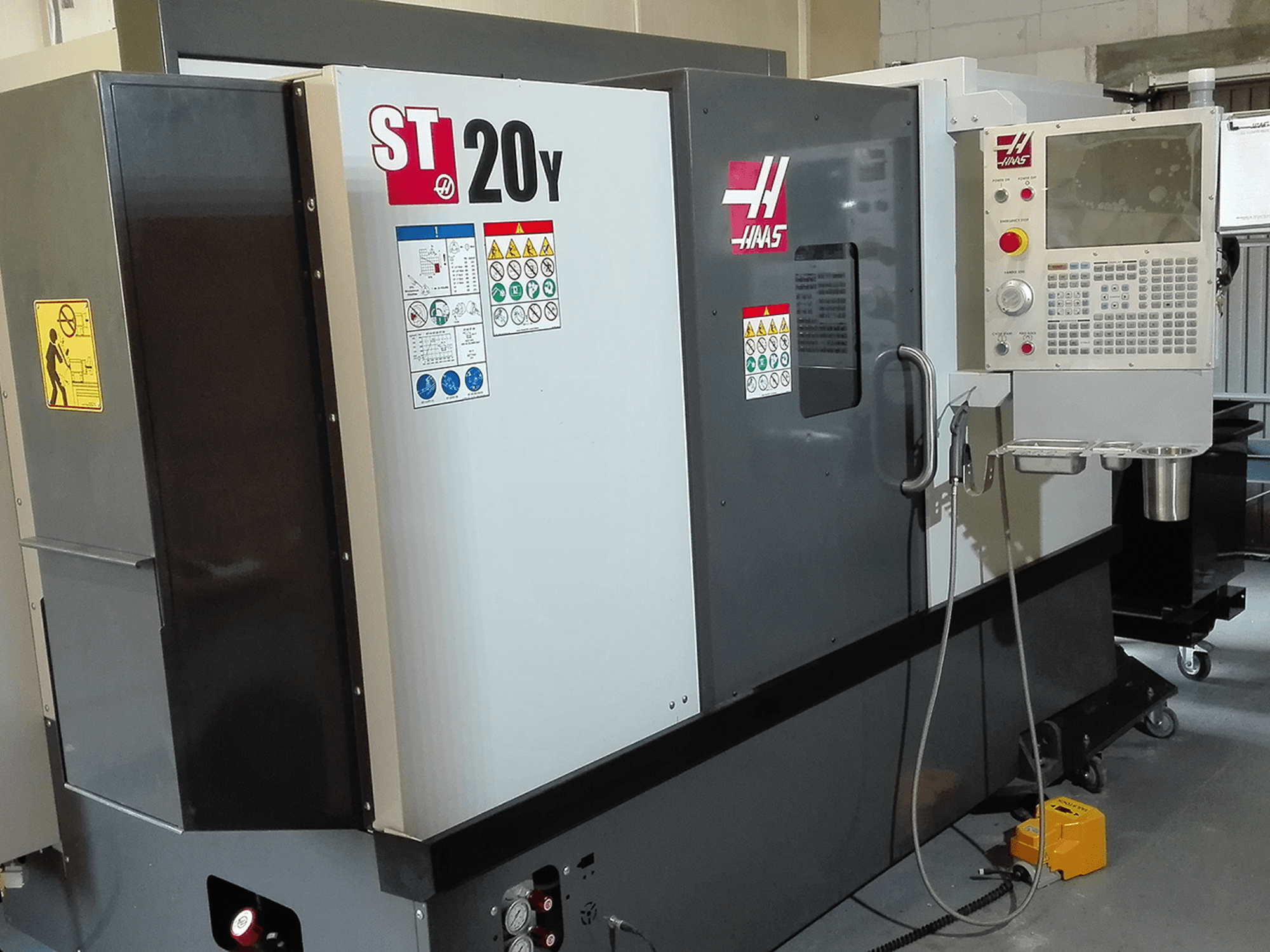 Haas ST20Y CNC torna tezgahının önden görünümü, çalışma paneli, güvenlik etiketleri ve soğutma sıvısı sistemi.