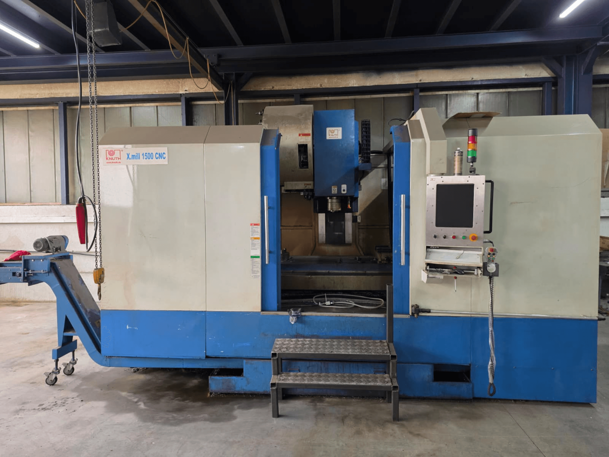 KNUTH X-MILL 1500 CNC dikey işleme merkezi, yandan görünüm; kontrol paneli, basamaklar ve çıkış konveyörünü göstermektedir.