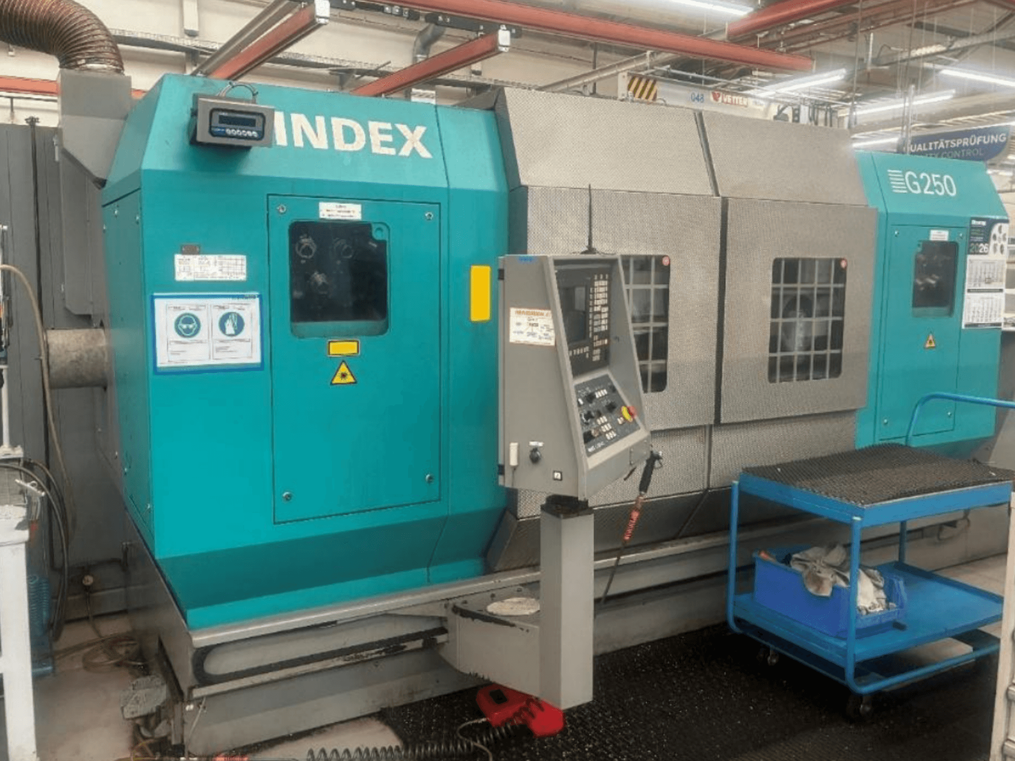 INDEX G250 yatay torna tezgahı; kontrol paneli ve metal gövdeyi gösteren önden görünüm, güvenlik etiketleri ve mavi bir taşıma arabası ile birlikte.