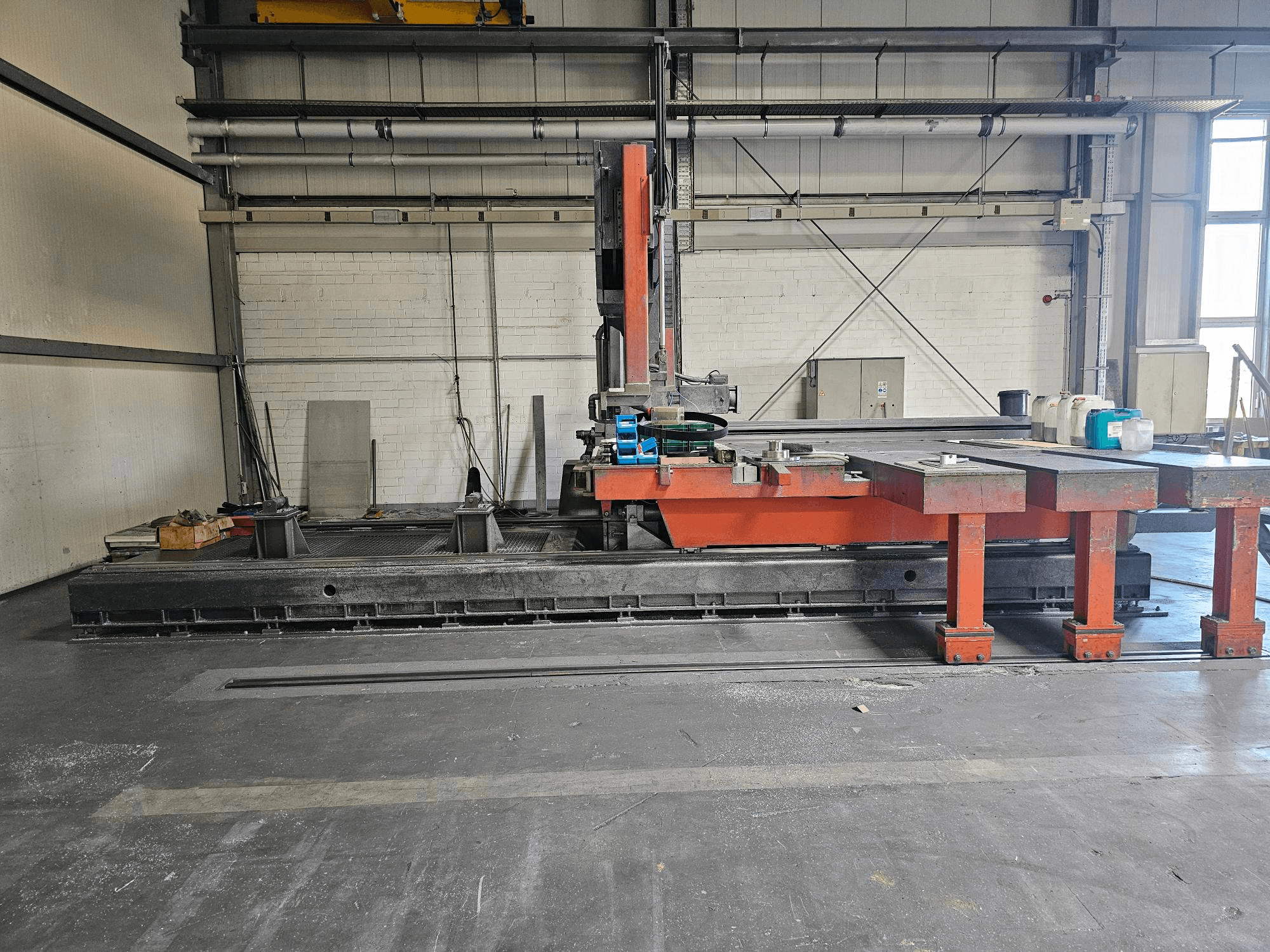 Açık bir atölyede endüstriyel kesim makinesi, turuncu ve siyah, büyük bir masa; aksesuarları ve çalışma alanını gösteren yandan görünüm.