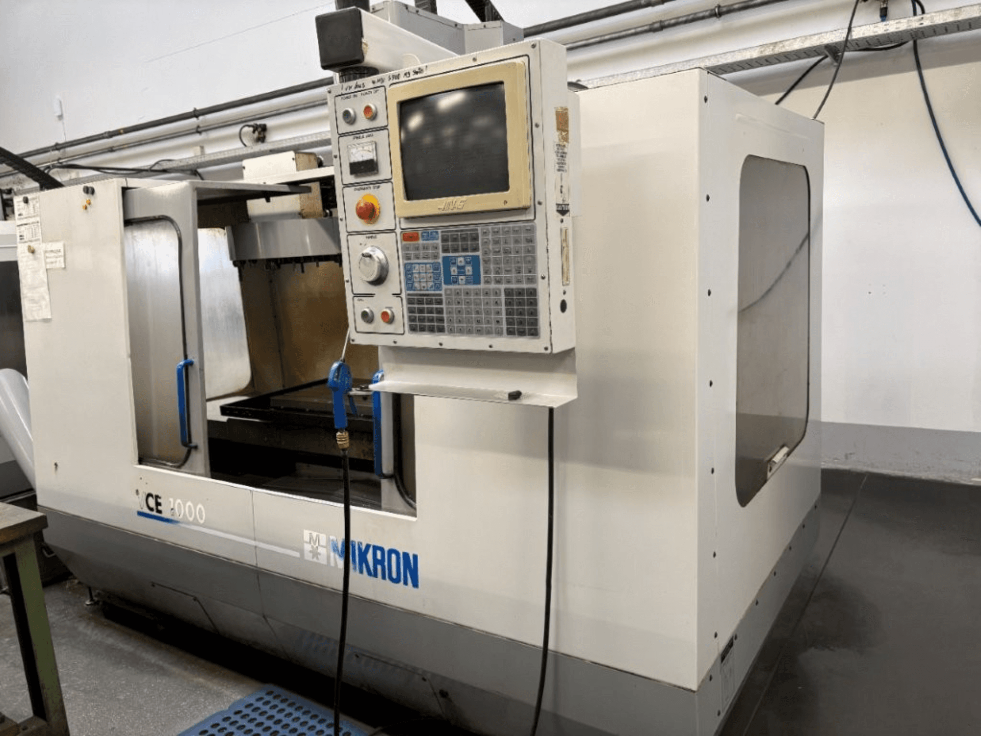 Mikron CE 2000 CNC makinesi, önden görünüm; düğmeli ve ekranlı bir kontrol paneli, gümüş dış yüzey ve çalışma alanına sahiptir.