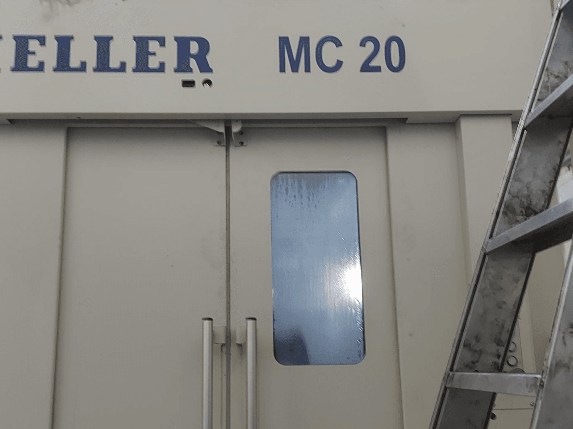 HELLER MC 20 yatay işleme merkezinin önden görünümü, kapı kollarını ve küçük bir pencereyi gösterir. Yan tarafta merdiven.
