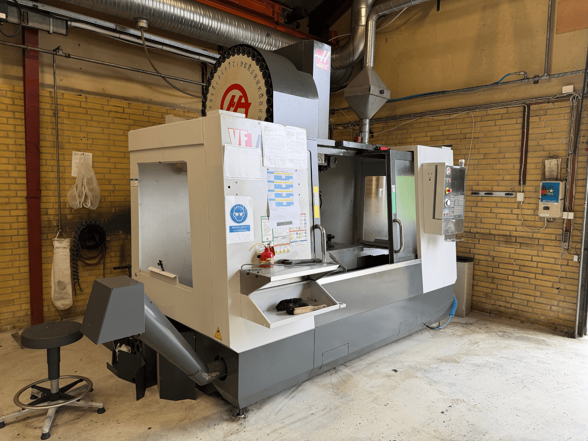 HAAS VF-4 Dikey İşleme Merkezi, önden görünüm; arka planda kontrol paneli, takım tutucu ve üretim düzeni görülmektedir.