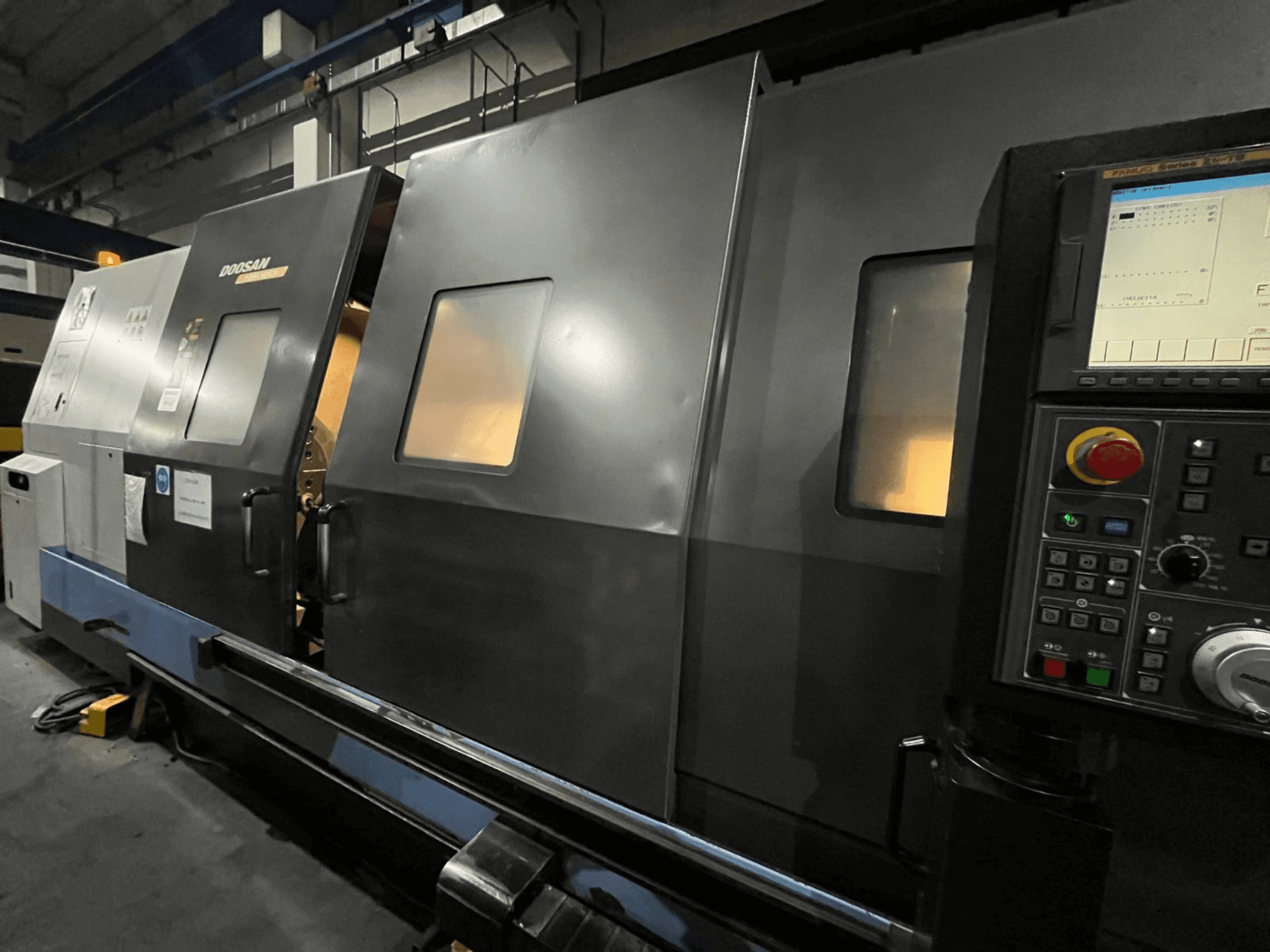Önden görünümlü Doosan CNC torna makinesi, görünür dijital ekran ve düğmelere sahip kontrol paneli ve operatör arayüzü.