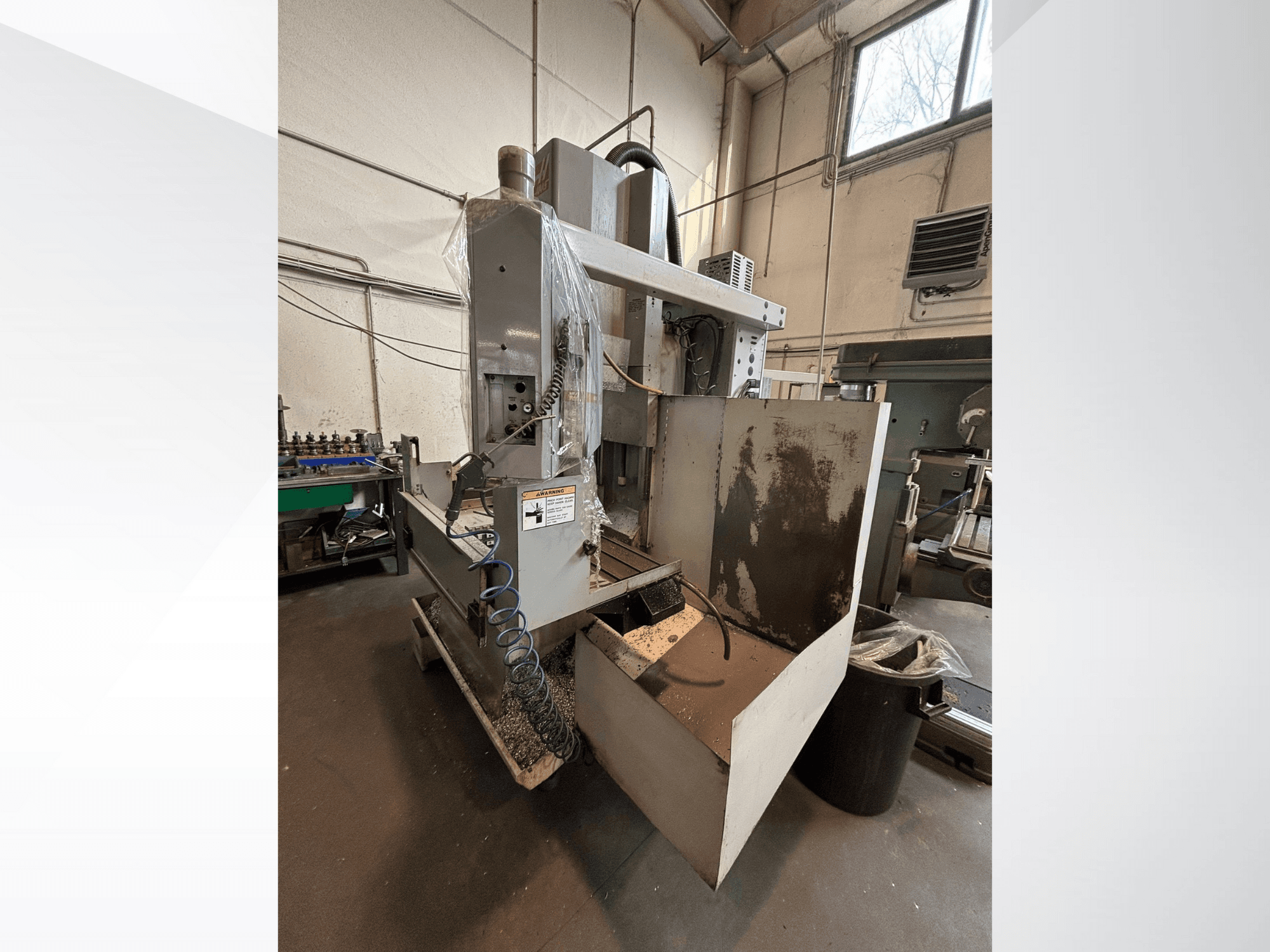 Koruyucu kapaklı dikey freze makinesi, yandan görünüm; soğutma suyu hortumu ve görünür kontrol paneli içerir. İşleme için idealdir.