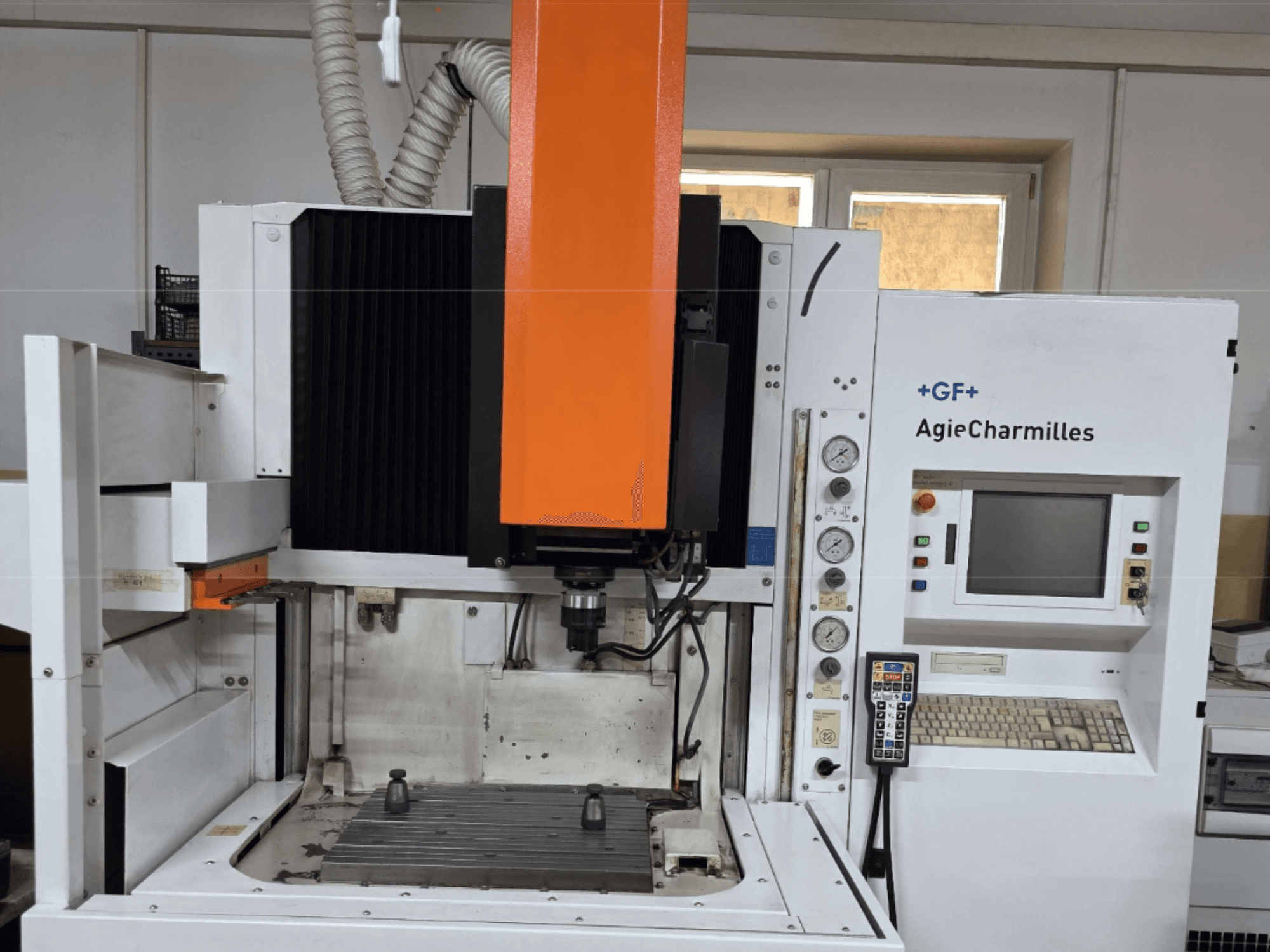 Büyük turuncu iş mili, kontrol paneli ve görünür çalışma masası ile önden görünümlü AgieCharmilles işleme merkezi.