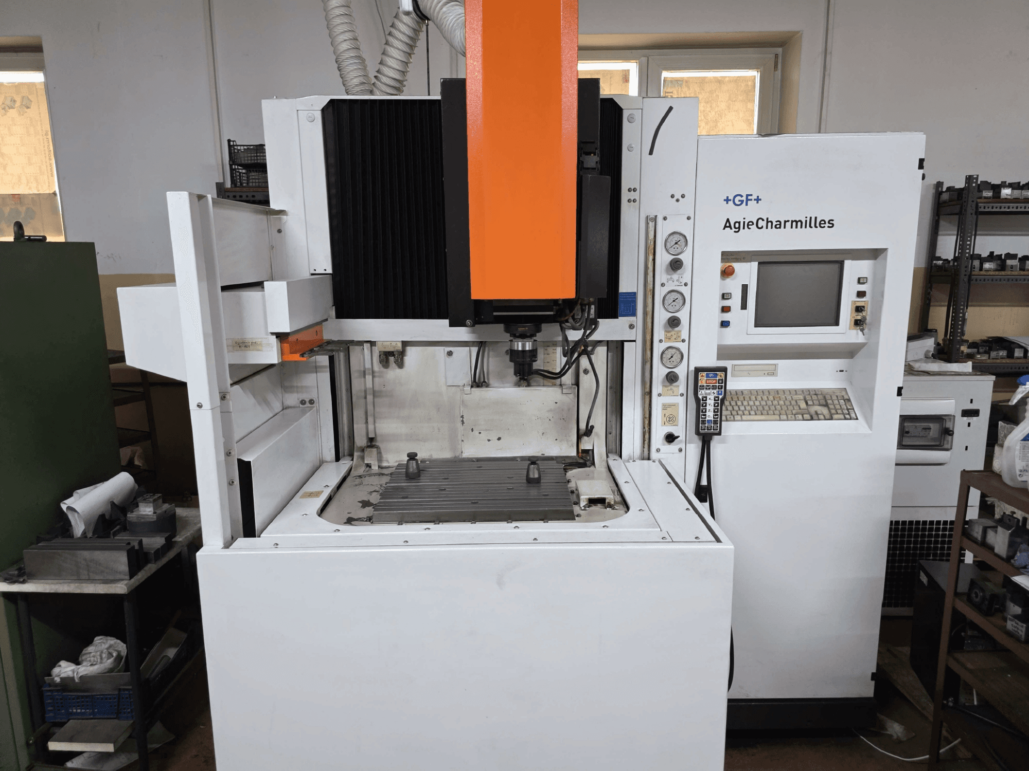 GF AgieCharmilles CNC makinesi, belirgin turuncu iş mili, dijital kontrol paneli ve monte edilmiş matkap tablası ile önden görünüm.