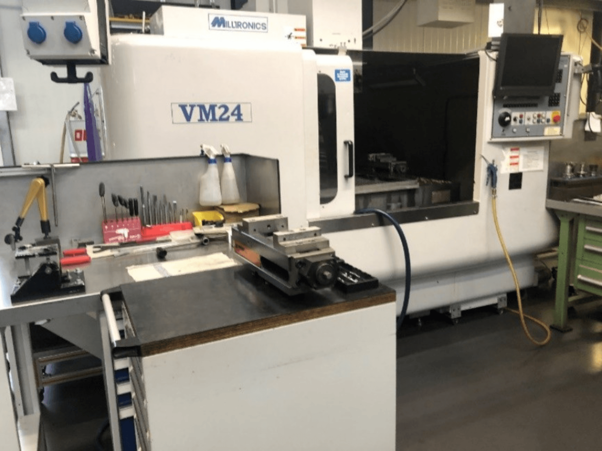 Milltronics VM24 CNC makinesini içeren makine çalışma alanı. Tezgah üzerindeki alet ve ekipmanlarla önden görünüm.