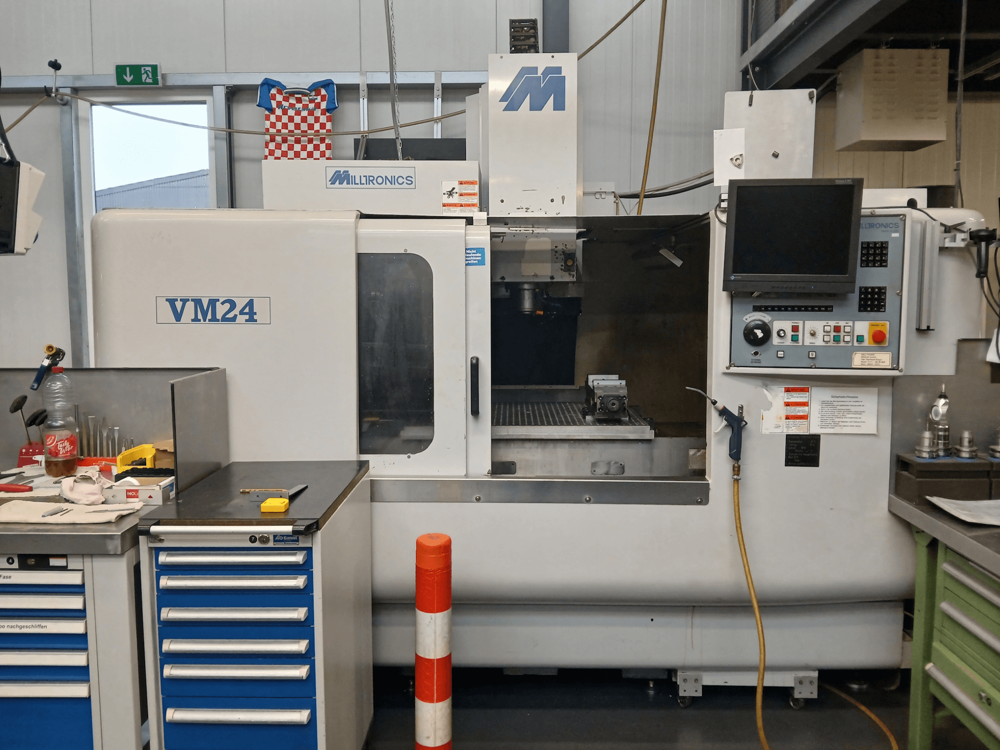 Milltronics VM24 CNC freze makinesi, kontrol paneli, takım depolama ve çalışma alanı kurulumu ile önden gösterilmiştir.