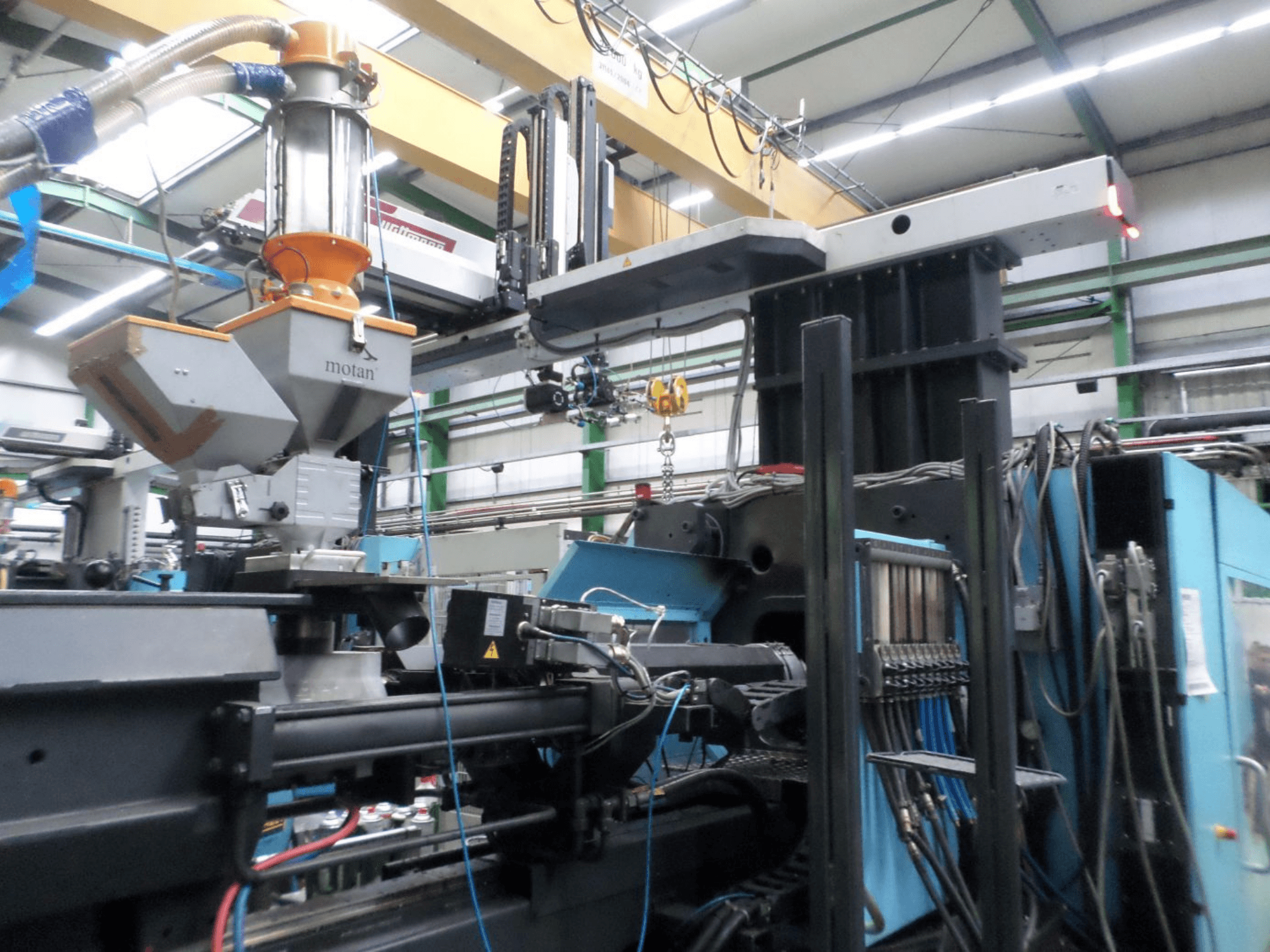 DEMAG D 1300 hidrolik enjeksiyon kalıplama makinesi, yan görünüm; fabrika ortamında hazne, kontrol ünitesi ve bağlantıların gösterildiği bir görüntü.