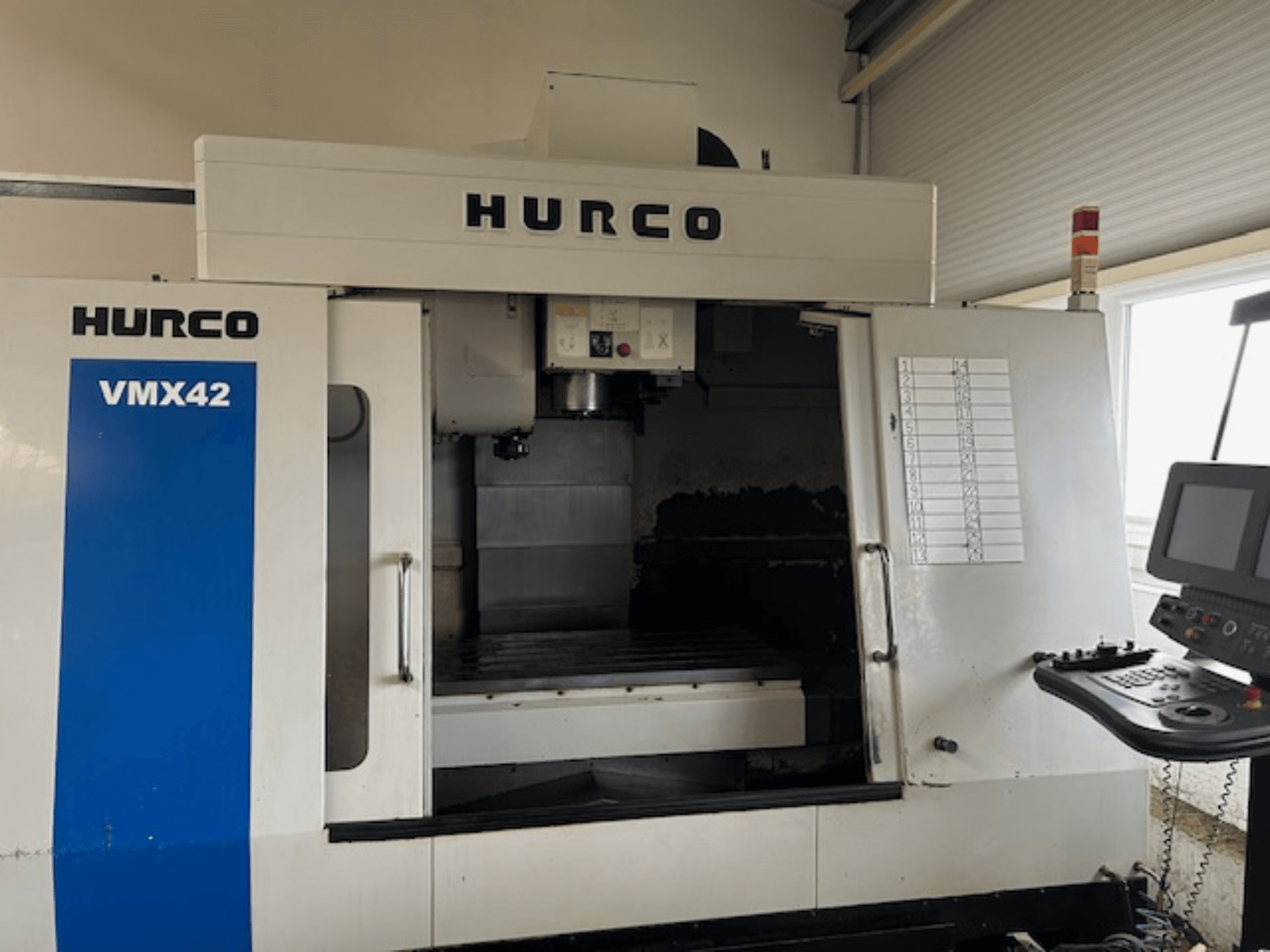 Hurco VMX42 CNC makinesinin önden görünümü, kontrol panelini, iş milini ve çalışma alanını gösterir; çalışma düzenini ortaya koyar.