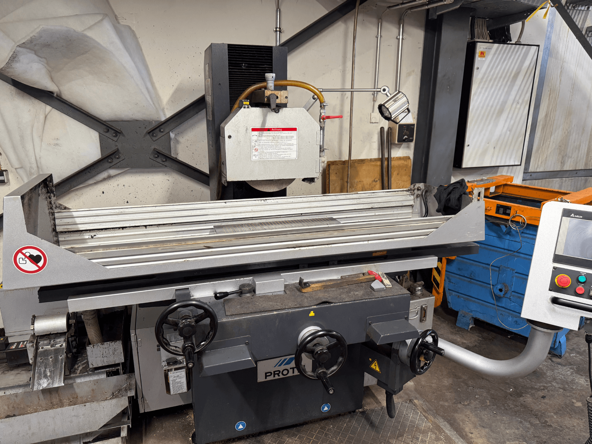 PROTEC makinesi, önden görünüm, manuel kontrolleri, güvenlik uyarıları ve soğutma sistemi olan bir yüzey taşlama makinesini göstermektedir.