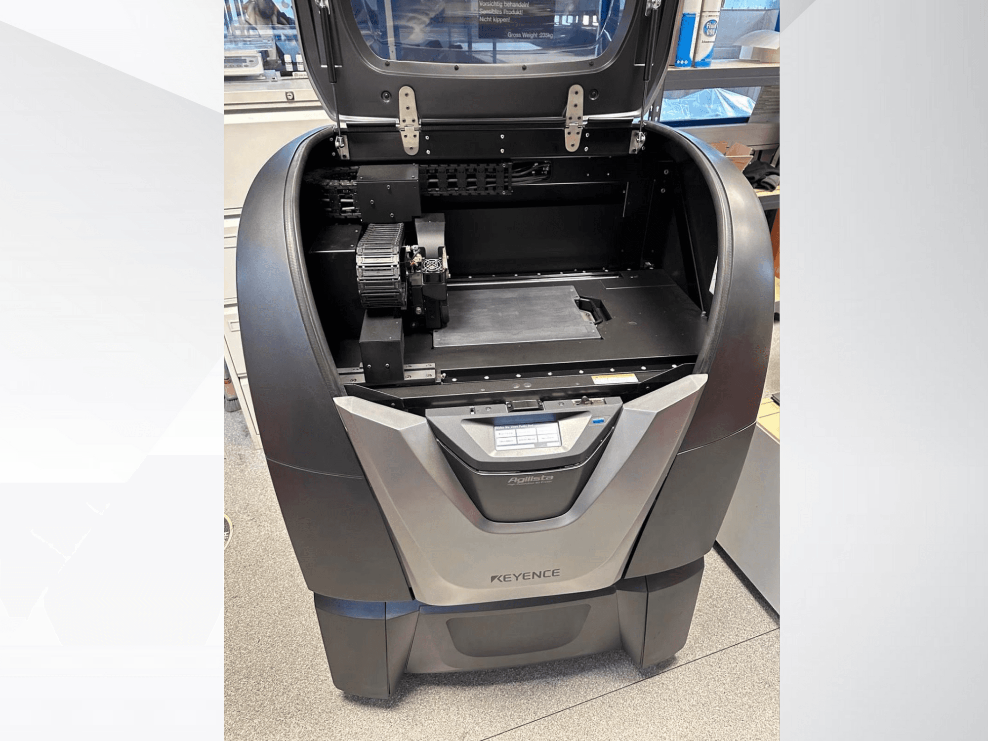 KEYENCE Agilista 3D yazıcı, önden görünüm, açık üst kısmı, geniş yapı platformunu ve dahili mekanik bileşenleri ortaya çıkarır.