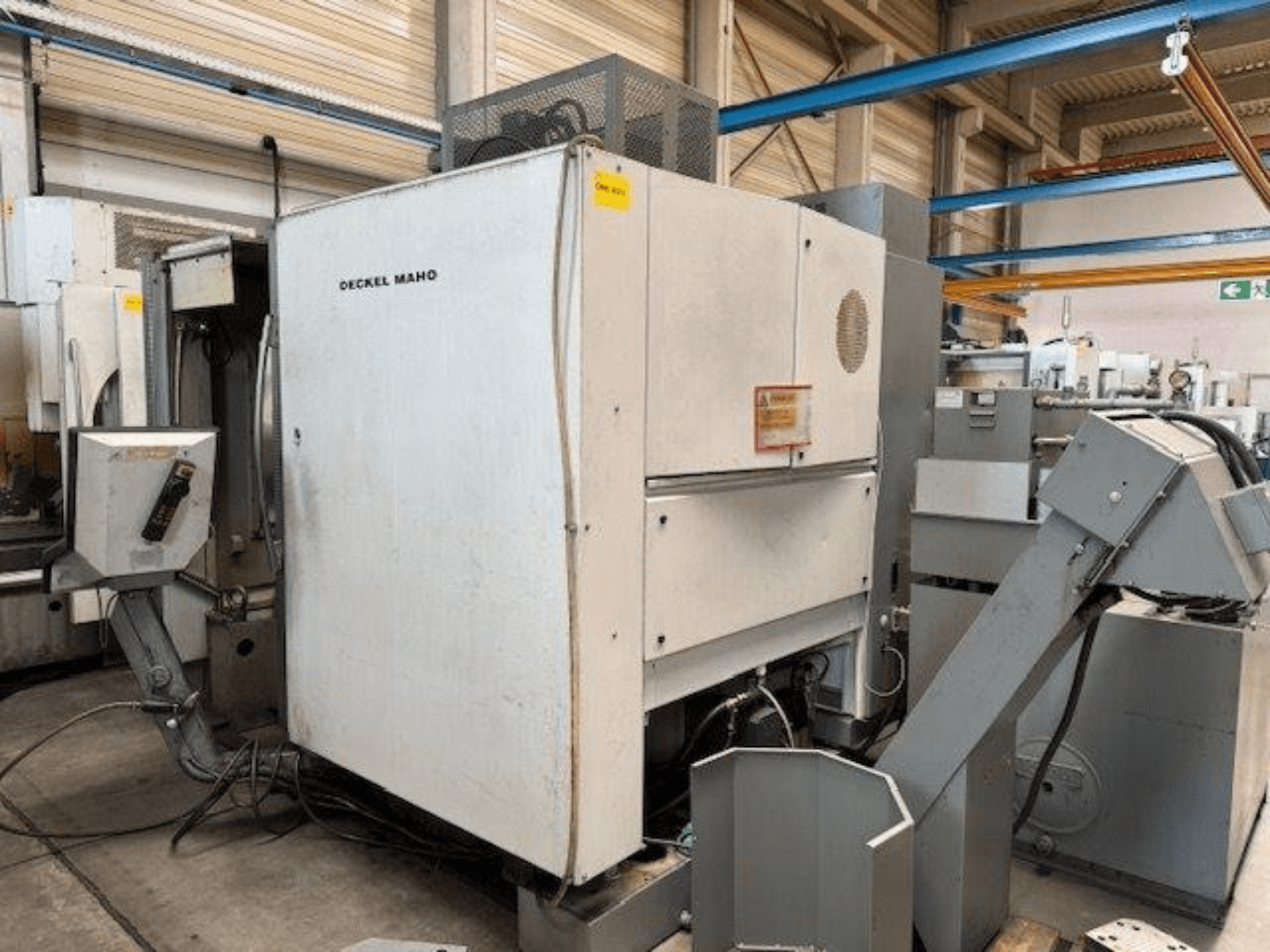 DECKEL MAHO DMC 100 V dikey işleme merkezi, kontrol paneli ve çeşitli ataşmanlar görünür şekilde yandan görünüm.