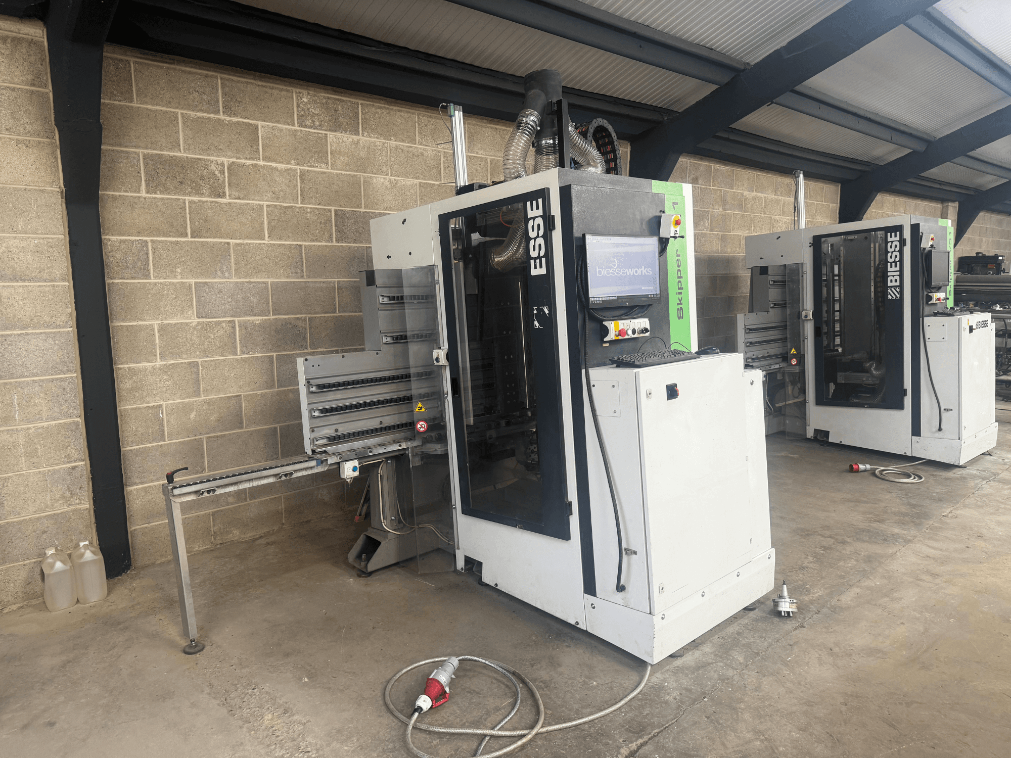 BIESSE Skipper v31 ahşap delme makinesinin yandan görünümü, kontrol paneli ve bitişik makineler, bir atölyede.