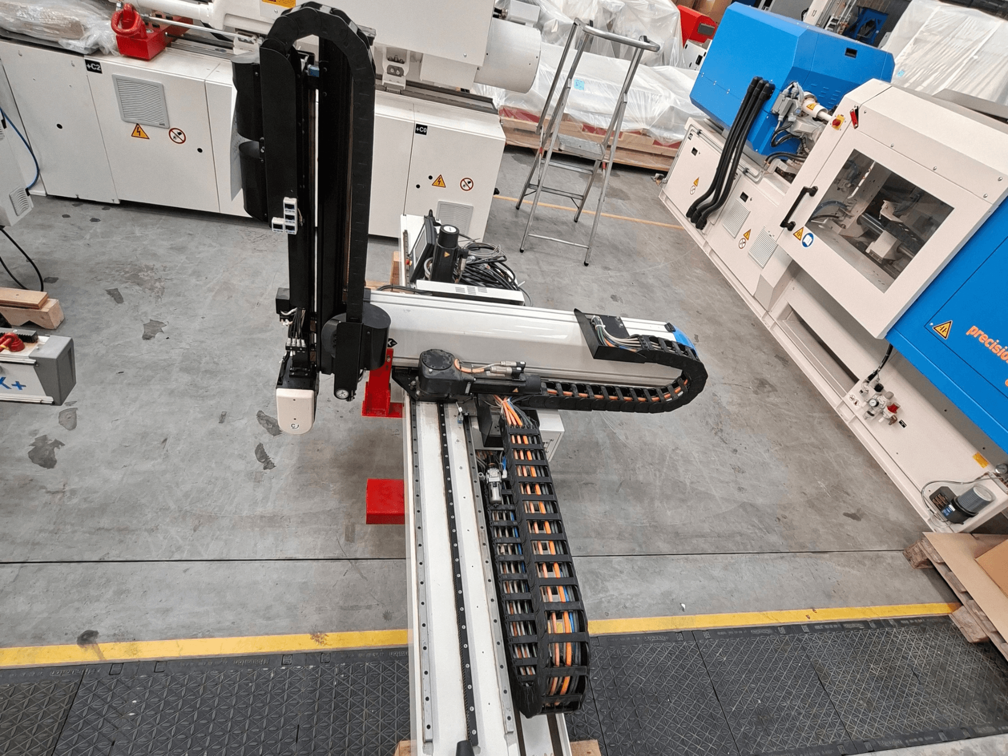 Krauss Maffei LRX150-MC5 plastik işleme makinesinin üstten görünümü; fabrika zeminindeki robot kolu ve kablo kanalı görülmektedir.