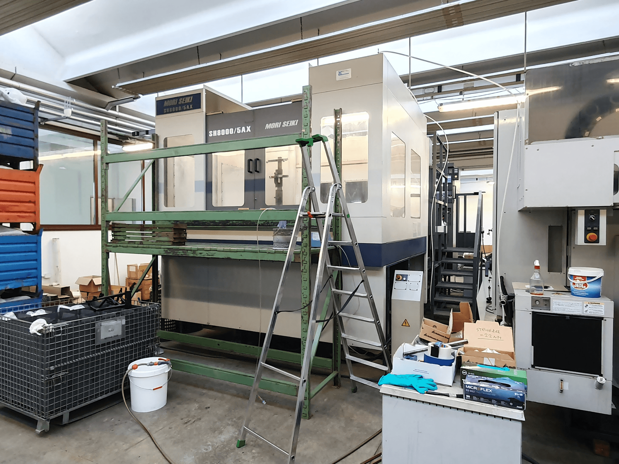 Mori Seiki SH-8000/5AX CNC makinesi bir atölyede, önden görünüm, atölye aletleri ve saklama kutuları yakında.