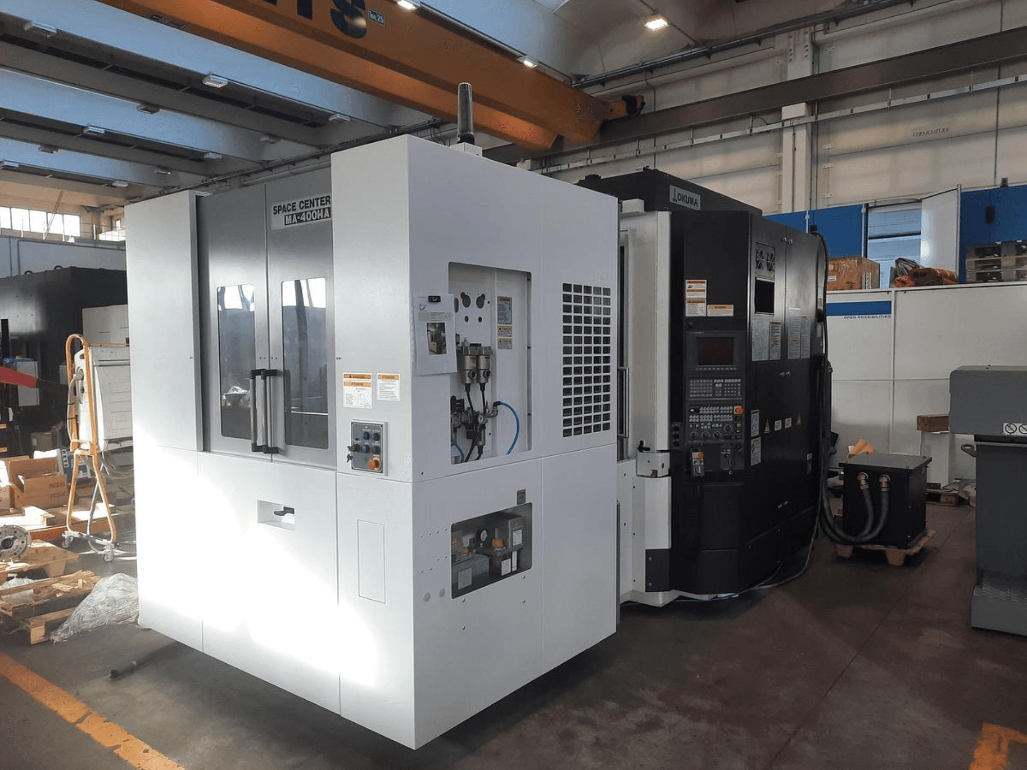 SPACE CENTER IM-400HAA ve OKUMA CNC makinelerinin önden görünümü, çeşitli kontrolleri ve üretici etiketlerini sergiliyor.