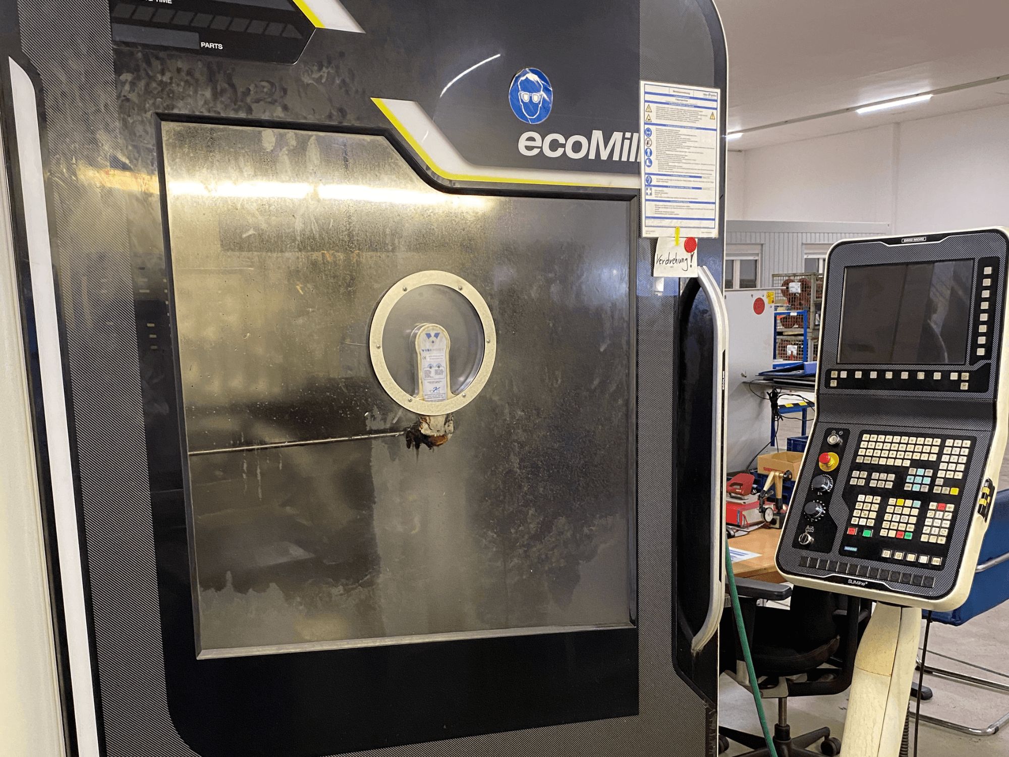 DMG MU 70 ECO Freze Makinesi’nin önden görünümü; sağ tarafta bir kontrol paneli ve iç bileşenleri gösteren bir cam panel bulunmaktadır.
