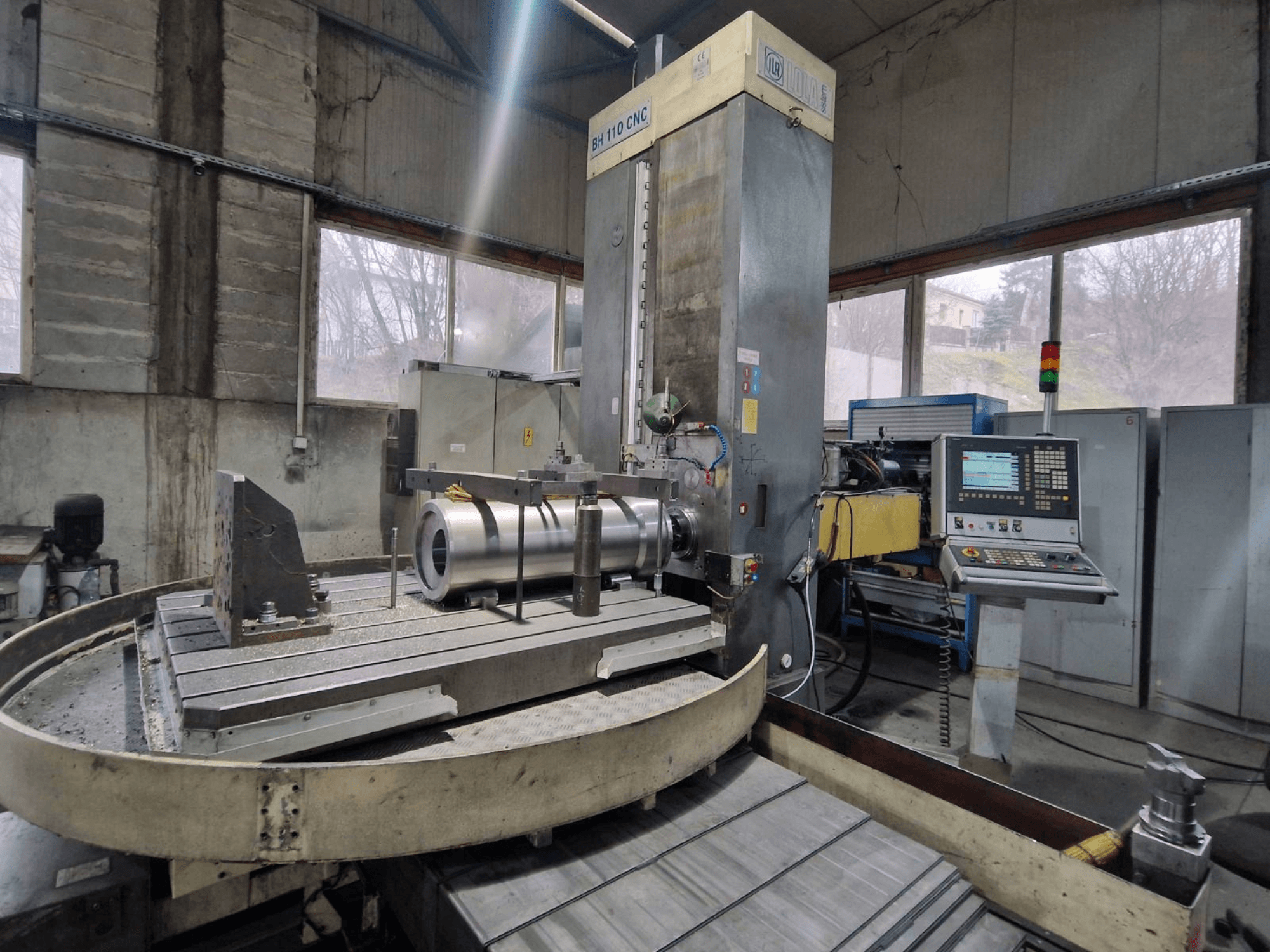 LOLA BH 110 CNC delme makinesi atölyede, önden görünüm, metal iş parçası ve kontrol paneli.