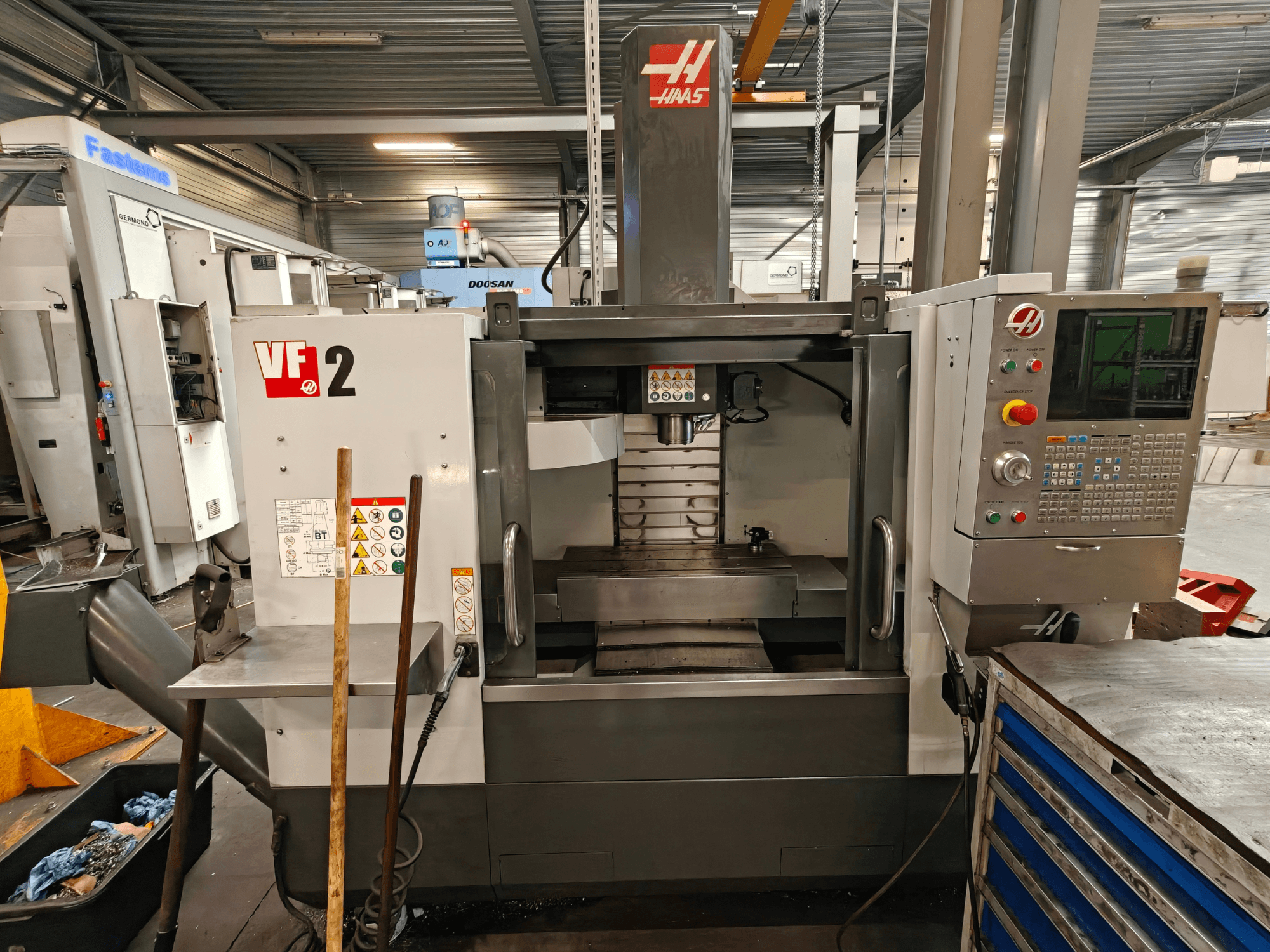 HAAS VF-2 Dikey İşleme Merkezi, önden görünüm; atölye ortamında kontrol paneli, iş mili ve iş masasını göstermektedir.