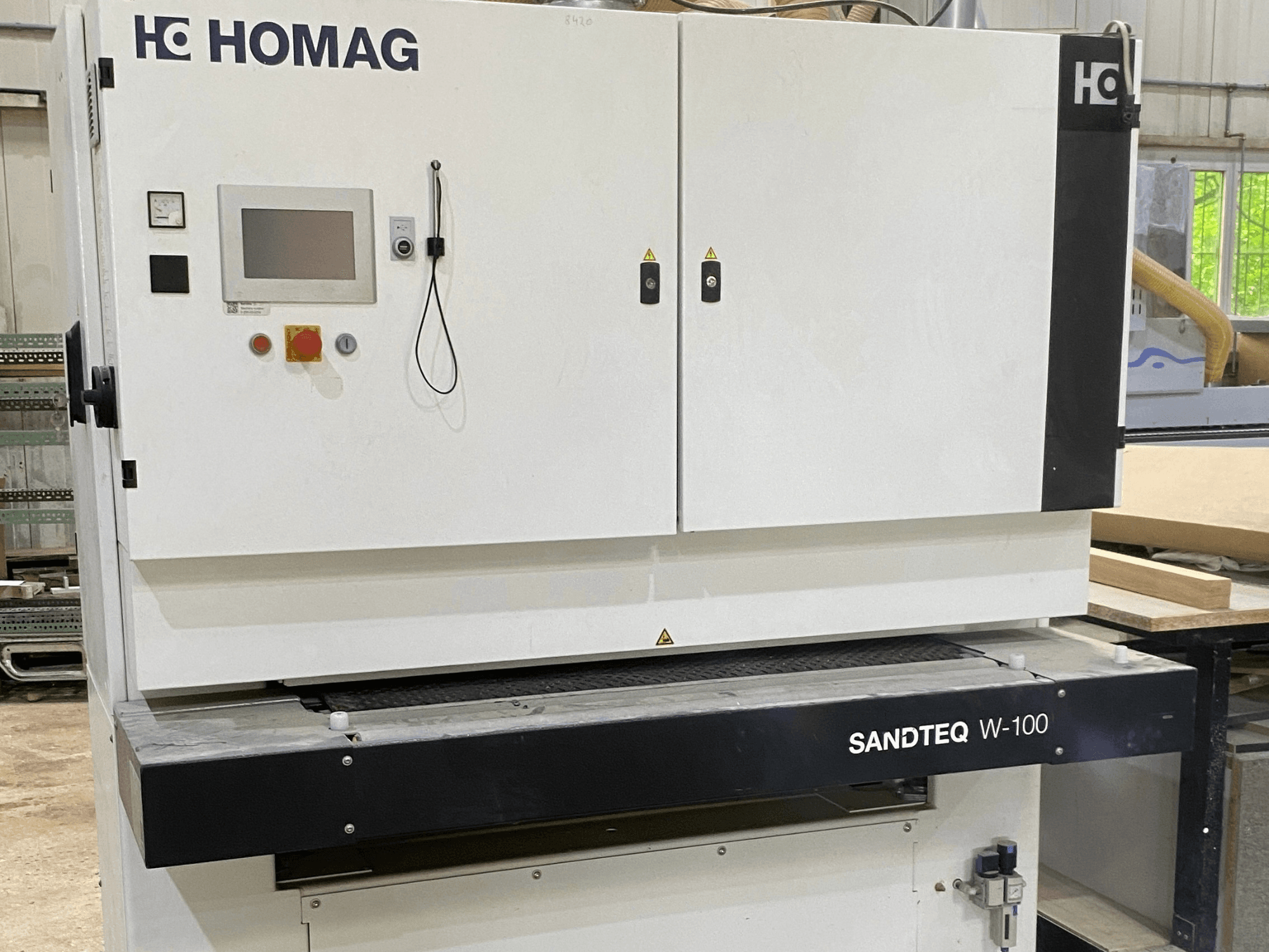 Bir atölyede bulunan HOMAG SANDTEQ W-100 bant zımpara makinesi; kontrol paneli, toz tahliye girişi ve zımpara bandı bölümü görülmektedir. Önden görünüm.