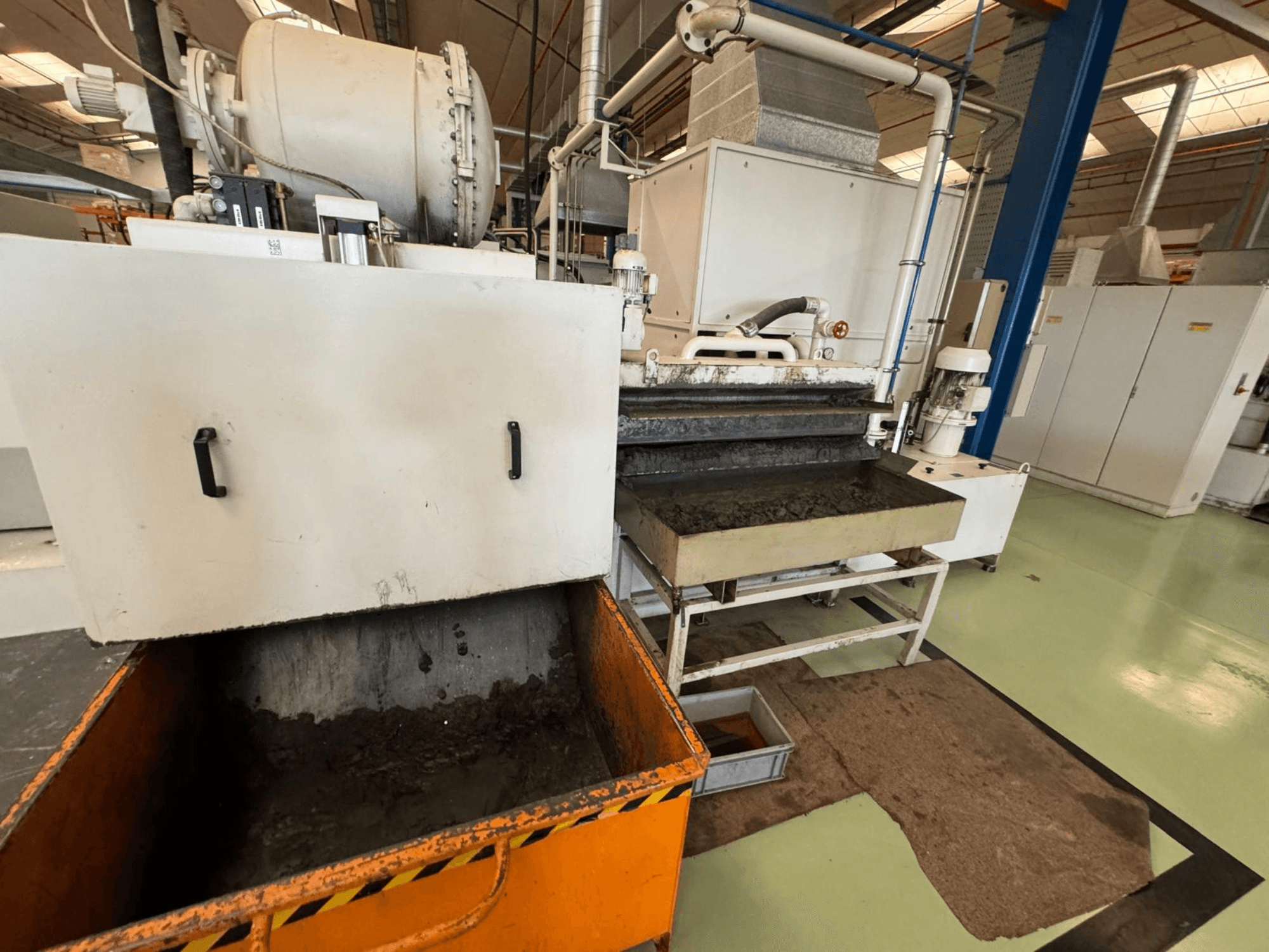 Turuncu bir atık kutusuna sahip endüstriyel işleme ekipmanı, önden görünüm; bir motor, konveyörler ve bakım alanı içerir.