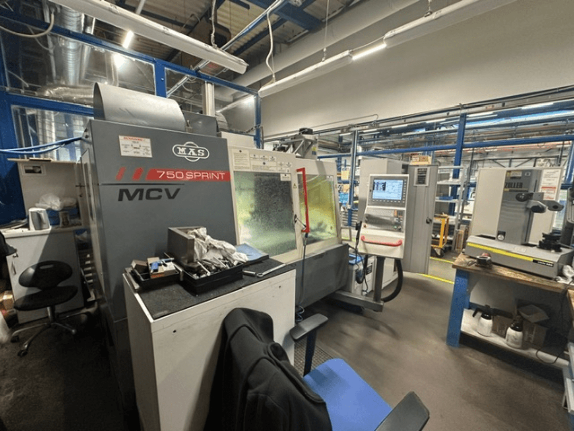 Bir atölyede bulunan KOVOSVIT MAS MCV 750 Sprint dikey işleme merkezi; yan görünümde kontrol paneli ve çalışma alanı gösterilmektedir.