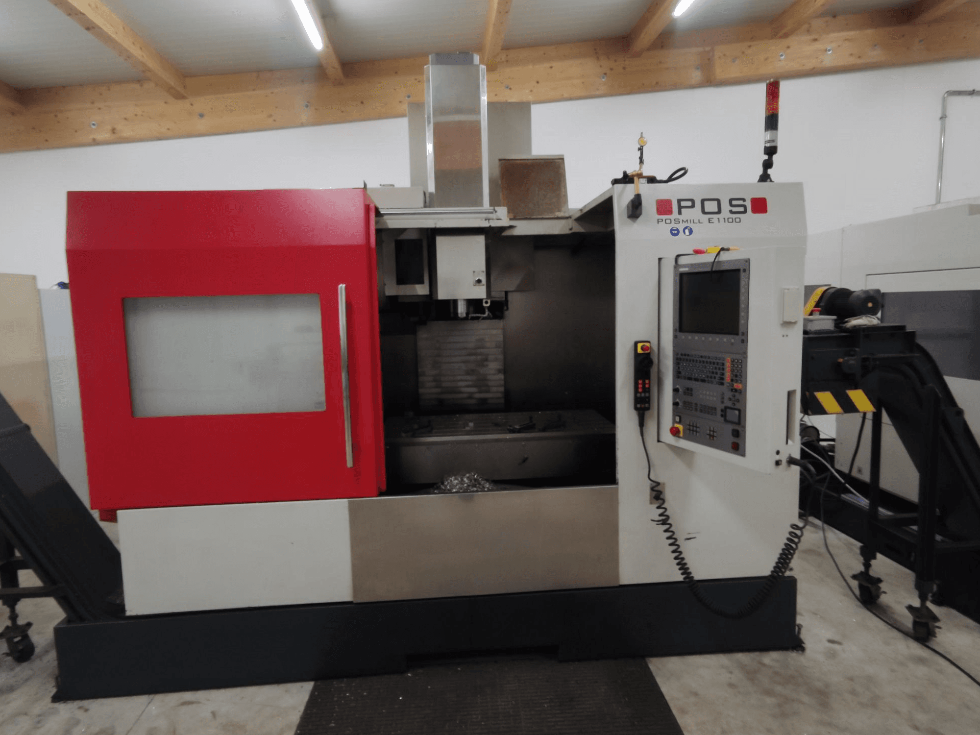 POS POSMILL E1100 CNC freze makinesinin kırmızı muhafazası, kontrol paneli ve üstündeki güvenlik ışığı ile önden görünümü.