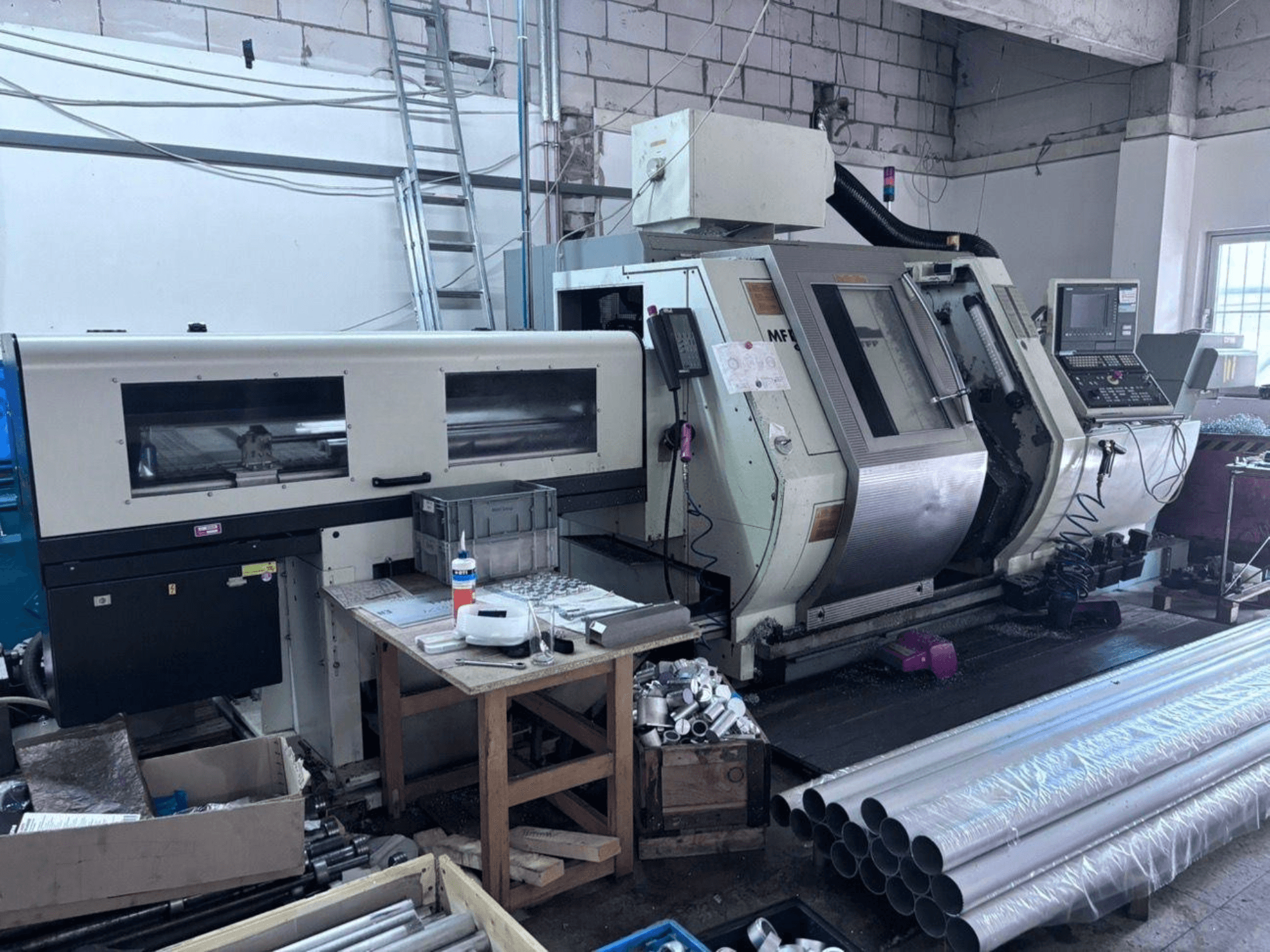 Gildemeister MF Twin 65 Torna-Frezleme Merkezi; kontrol paneli, işleme alanı ve alüminyum boruları gösteren yan görünüm.