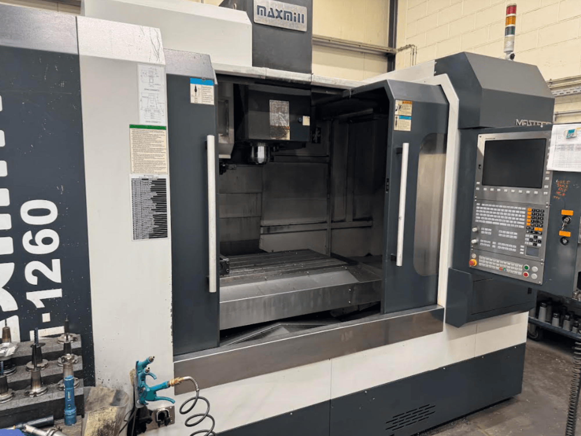 Maxmill CNC freze makinesi, model M-1260, kontrol paneli ve çalıştırma talimatları ile boş çalışma alanını gösteren önden görünüm.
