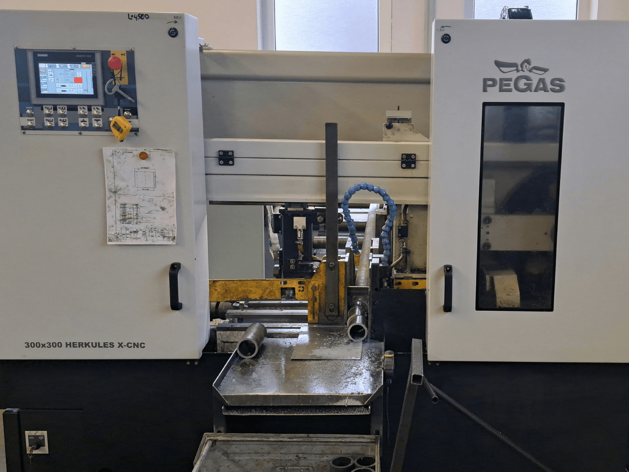Pegas HERKULES X-CNC 300x300 sac işleme makinesi, önden görünüm; kontrol paneli ve metal parçaların bulunduğu çalışma alanı gösterilmektedir.