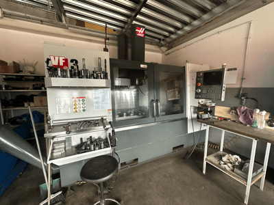 Atölyede Haas VF-3 CNC makinesi, bitişik masada takımlar ve kontroller ile önden görünüm, teknik arayüz ve güvenlik bilgileri görüntüleniyor.