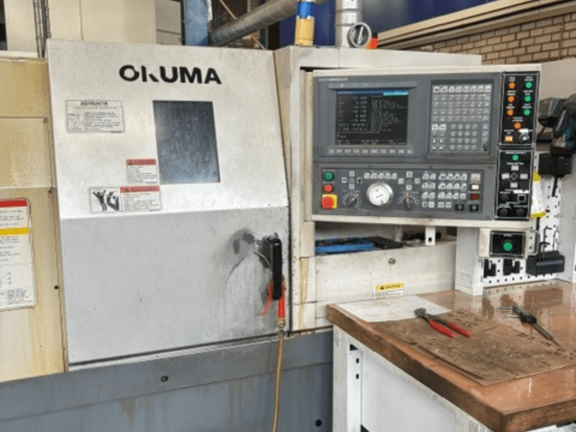 Okuma ES-L10II yatay torna tezgahının önden görünümü; kontrol paneli, ekran ve takımların bulunduğu çalışma alanı görülmektedir.