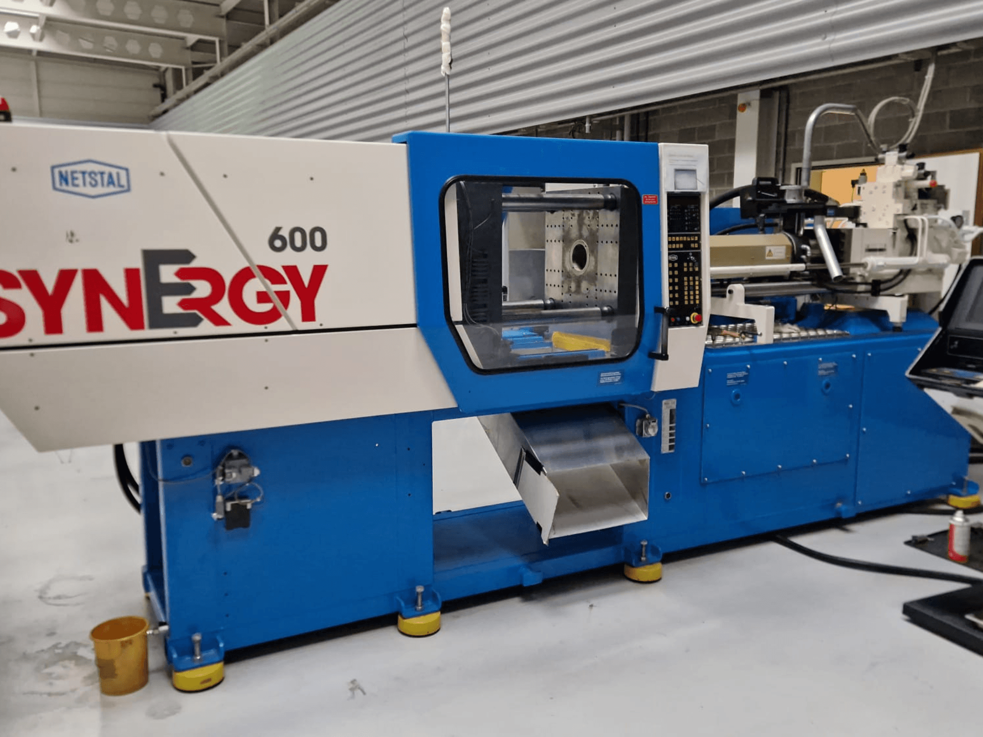 Netstal Synergy 600-230 hidrolik enjeksiyon kalıplama makinesi, kontrol paneli ve enjeksiyon alanını gösteren yandan görünüm.