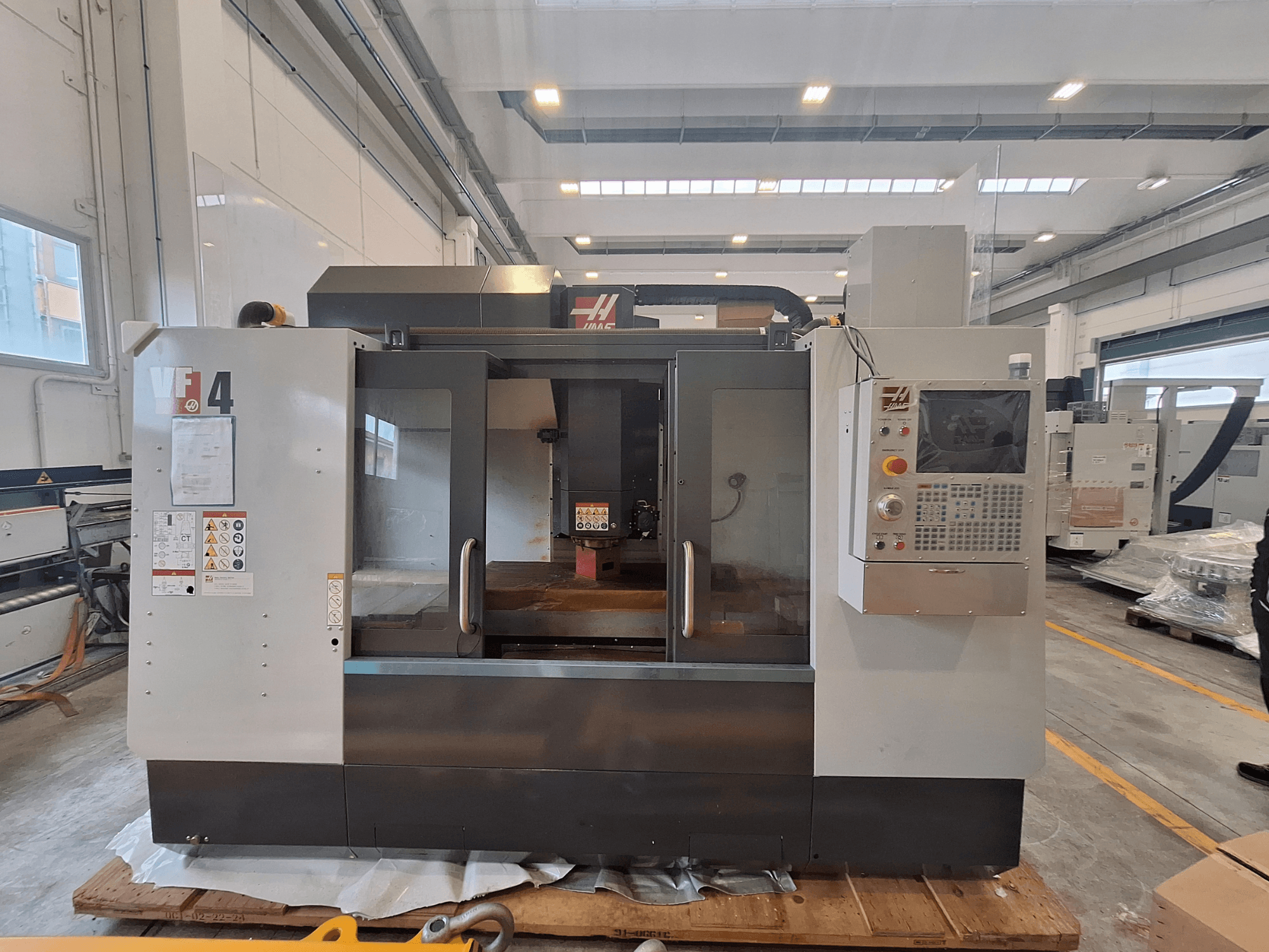 HAAS VF-4 dikey işleme merkezi, önden görünüm; depo ortamında kontrol paneli, çalışma alanı ve güvenlik etiketlerini göstermektedir.