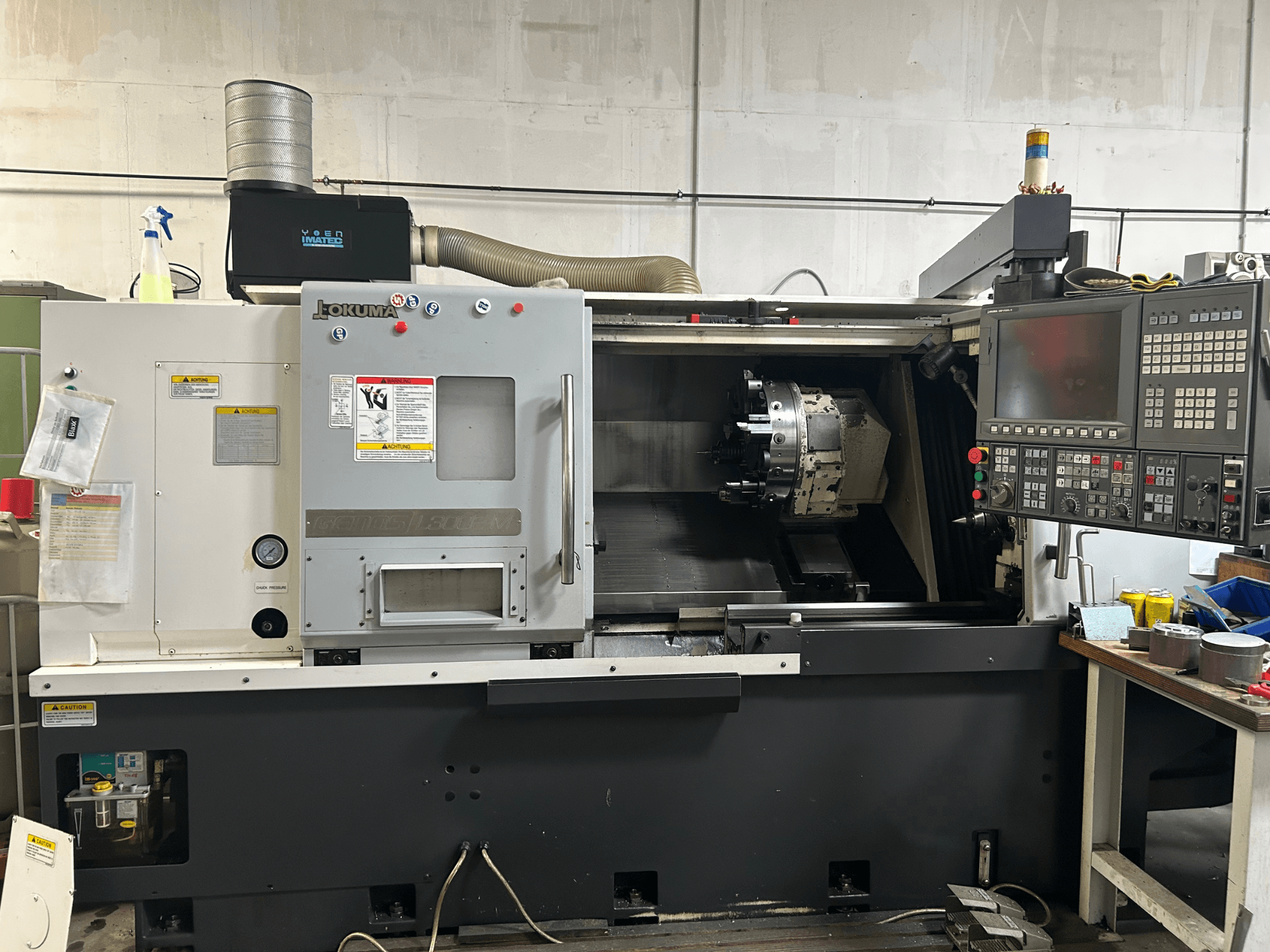 Okuma Genos L300E-M yatay torna makinesinin kontrol paneli, görünür iş mili ve çeşitli kurulum araçları ile önden görünümü.