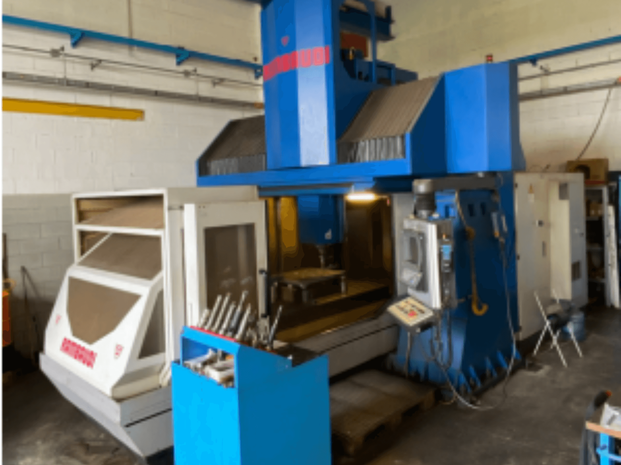 Dikey işleme merkezi Rambaudi RF103, kontrolleri, takım deposunu ve işleme alanını gösteren önden görünüm. Mavi ve beyaz dış yüzey.