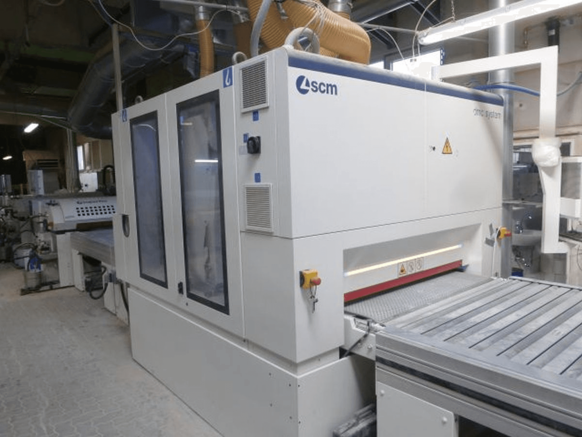 Bir atölyede bulunan SCM DMC SY TC 1350 bant zımpara makinesi; kontrol paneli ve güvenlik özelliklerine sahip zımparalama yüzeyini gösteren yan görünüm.