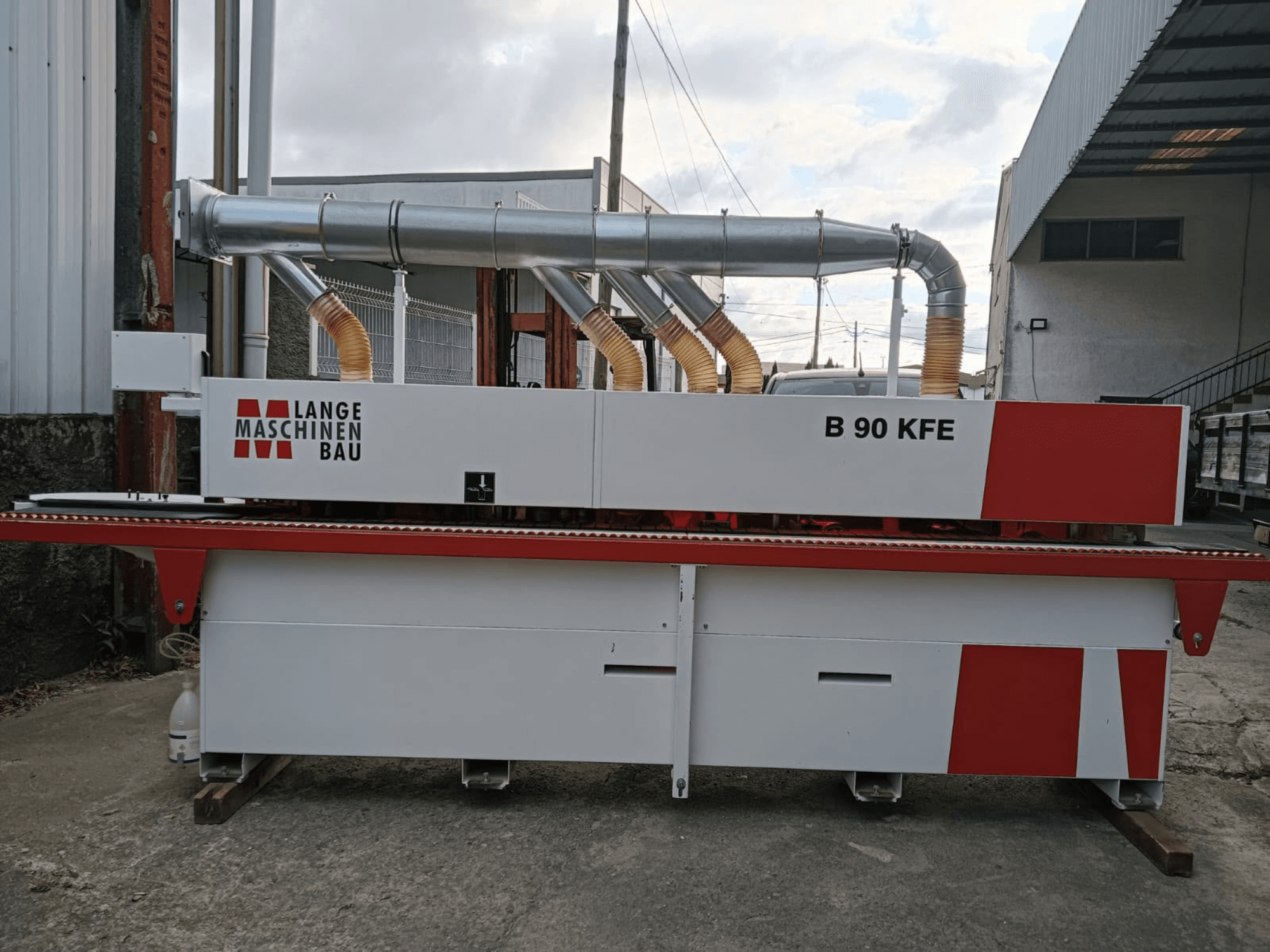 Endüstriyel bir çalışma alanında yer alan, çift egzoz borusu ve kırmızı detaylara sahip LANGE Maschinenbau B 90 KFE kenar kaplama makinesinin yandan görünümü.