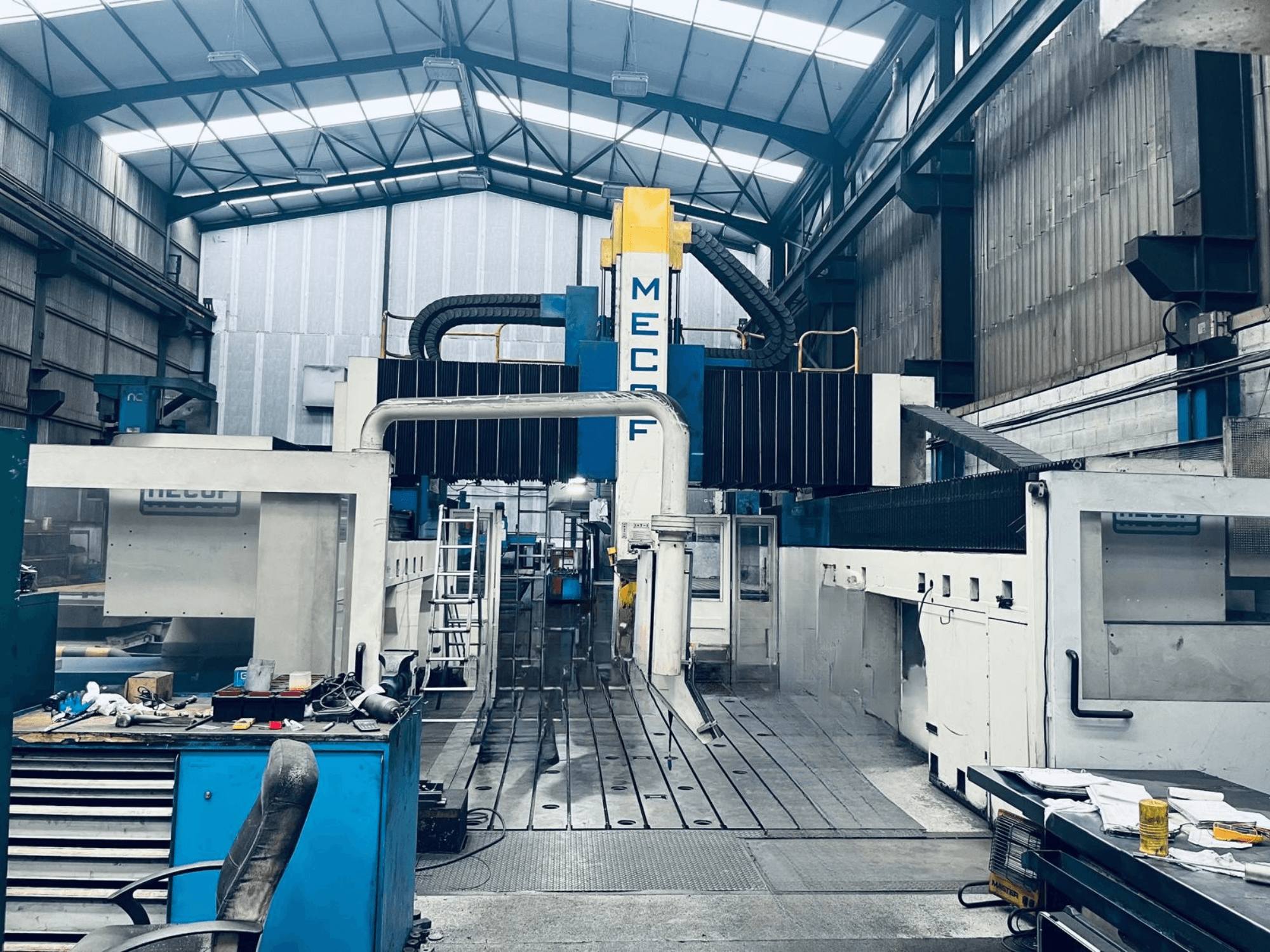 Atölyede bulunan MECOF DYNAMILL 3000L portal freze tezgahı, önden görünüm; mavi ve beyaz gövde, takımlar ve çalışma alanı görülmektedir.