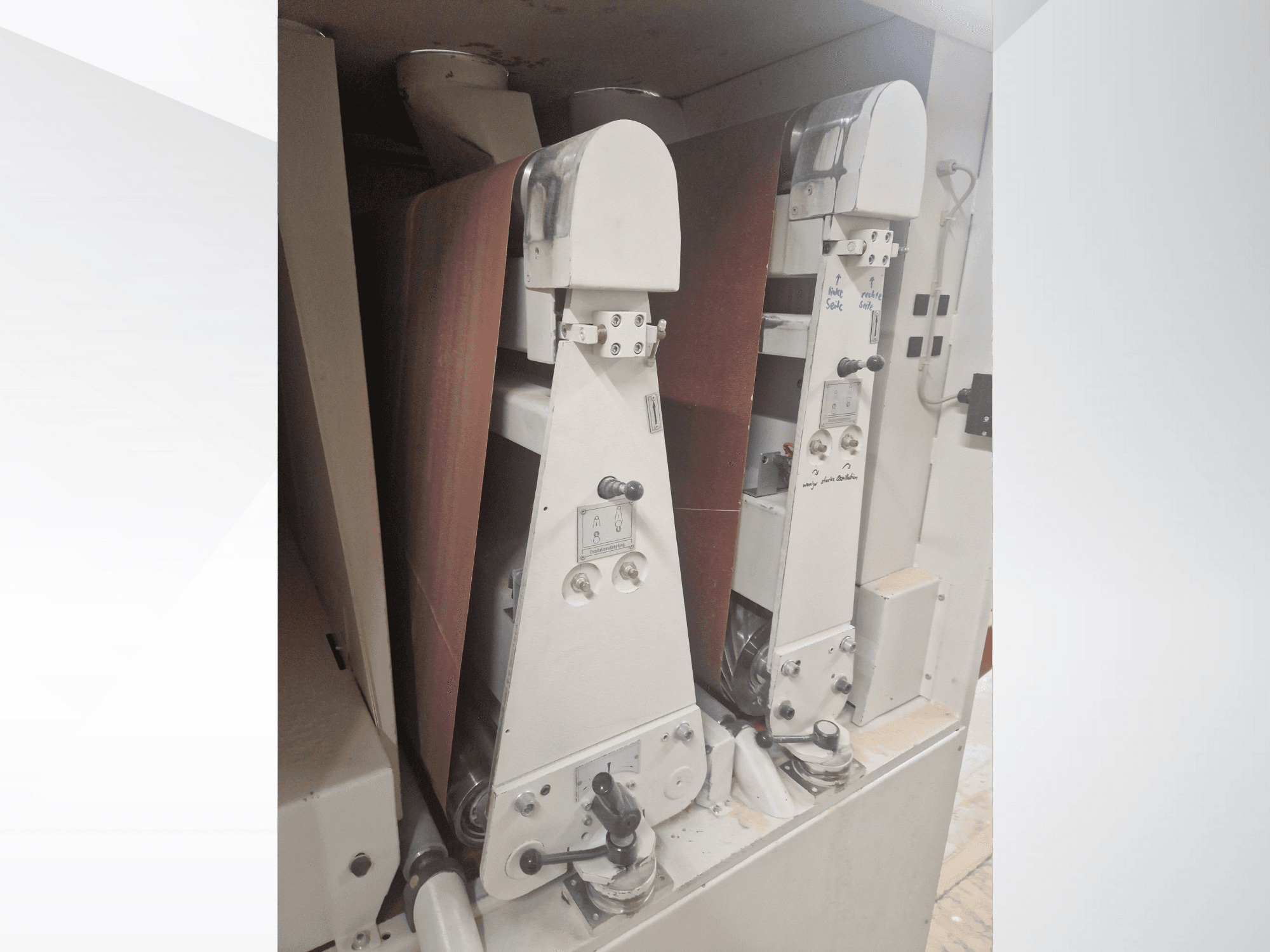 Kırmızı zımpara bantlı iki endüstriyel zımpara makinesi, önden görünüm, kontrolleri ve metalik bileşenleri sergiliyor.