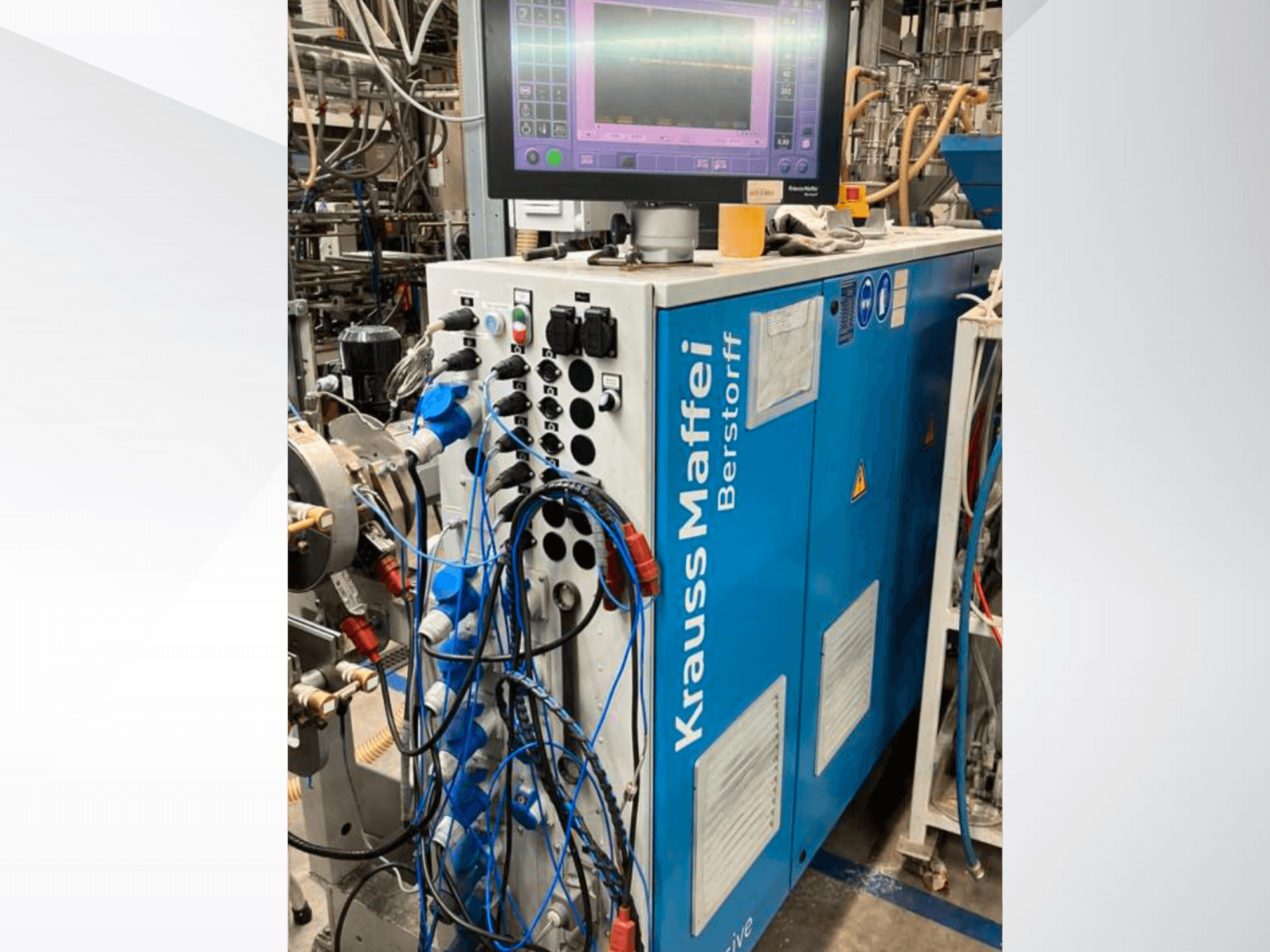 Krauss Maffei Berstorff kontrol panelli ve monitörlü endüstriyel makine, çeşitli düğmeler ve bağlı hortumlar, yandan görünüm.