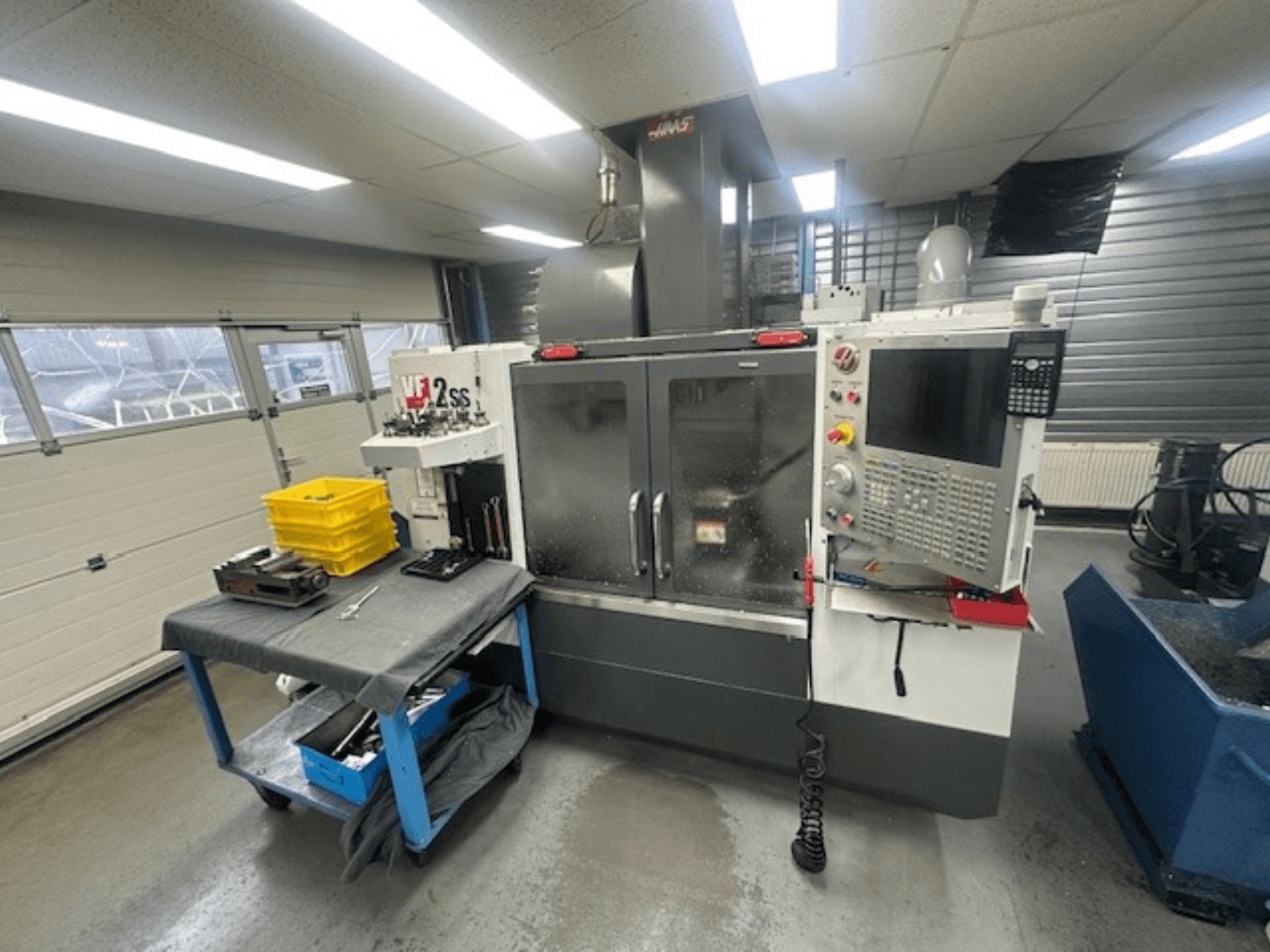 HAAS VF-2SS dikey işleme merkezinin kontrol paneli, çalışma tezgahı ve takım depolama istasyonu ile önden görünümü.